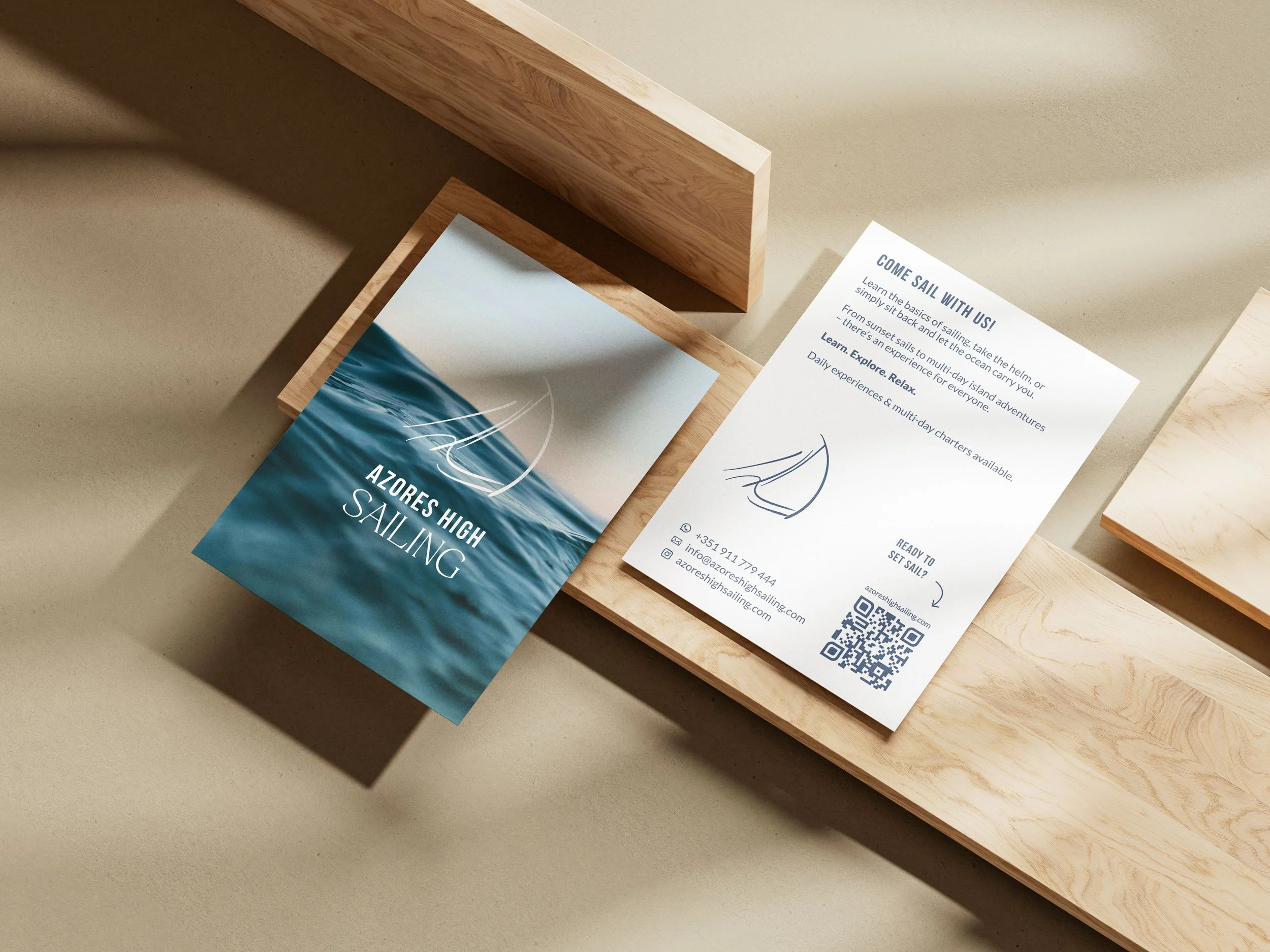 Flyer und Broschüren auf einem Holzregal, informieren über Segeln in den Azoren, mit Kontaktinformationen und QR-Code.