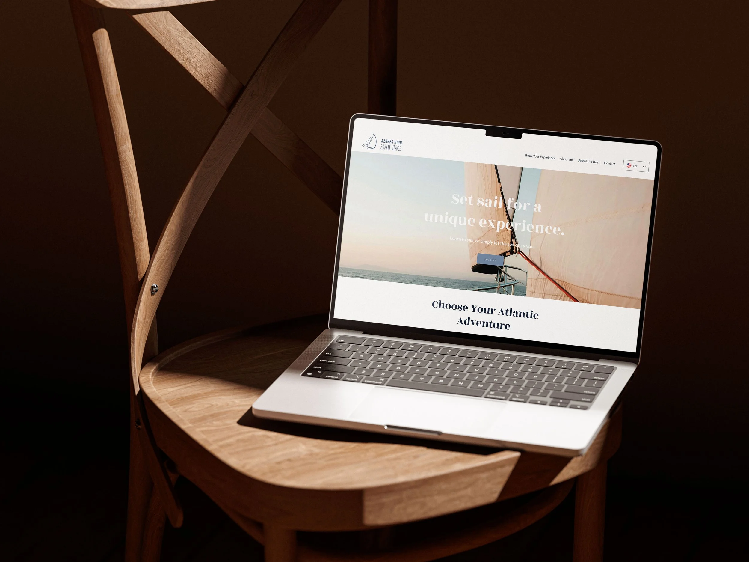 Ein Laptop auf einem runden, holzfarbenen Nachttisch mit einer Website für Segeltörns, der Text sagt 'Set sail for a unique experience'.
