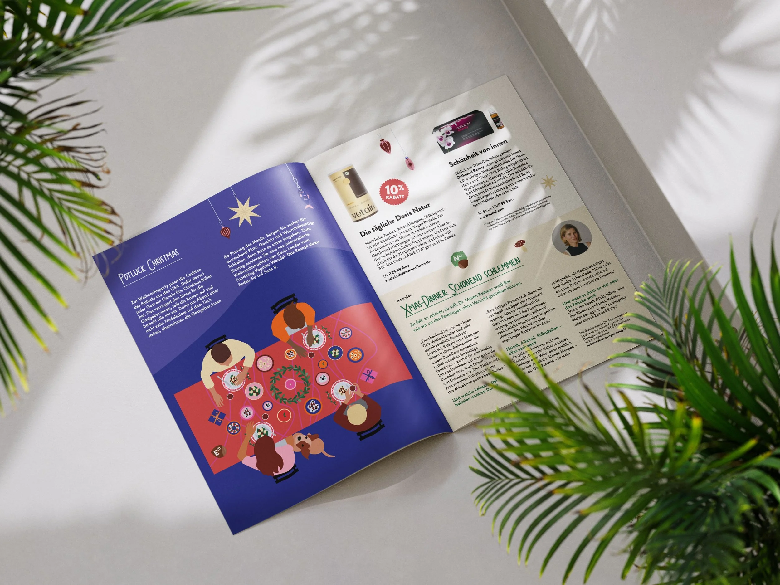 Ein aufgeschlagenes Magazin mit Weihnachts- und Festtagsdesign, das im Mittelpunkt eine Illustration von Personen zeigt, die um einen festlich gedeckten Tisch sitzen und gemeinsam essen, mit Tannenzweigen im Vordergrund und Schatten von Blättern an der Wand im Hintergrund.