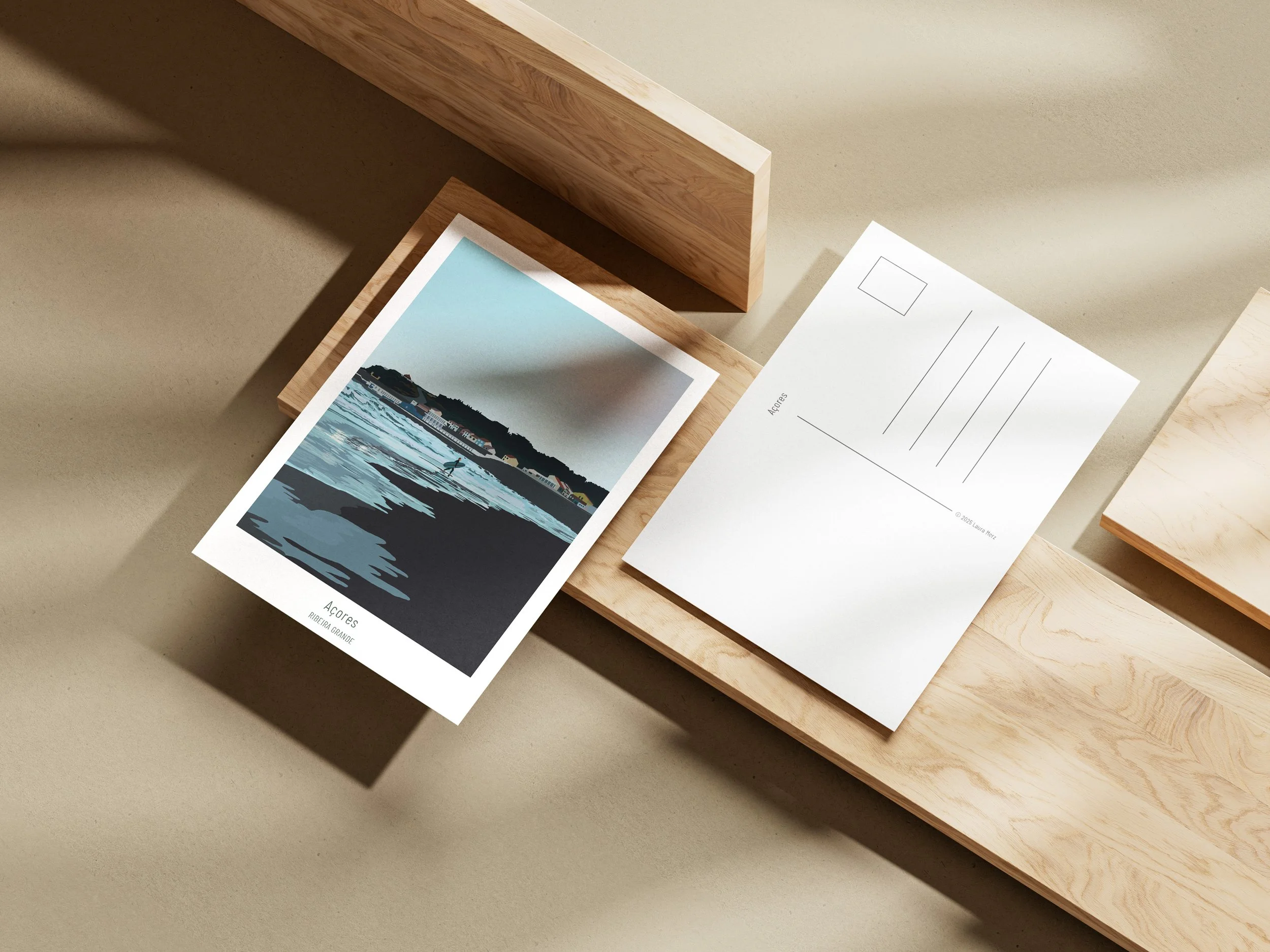 Foto von Postkarten oder Drucken auf einem Holztisch, mit einer zugeklappten Karte und einer Karte mit Illustration des Ozeans und der Küste, Beschriftung 'Açores'.