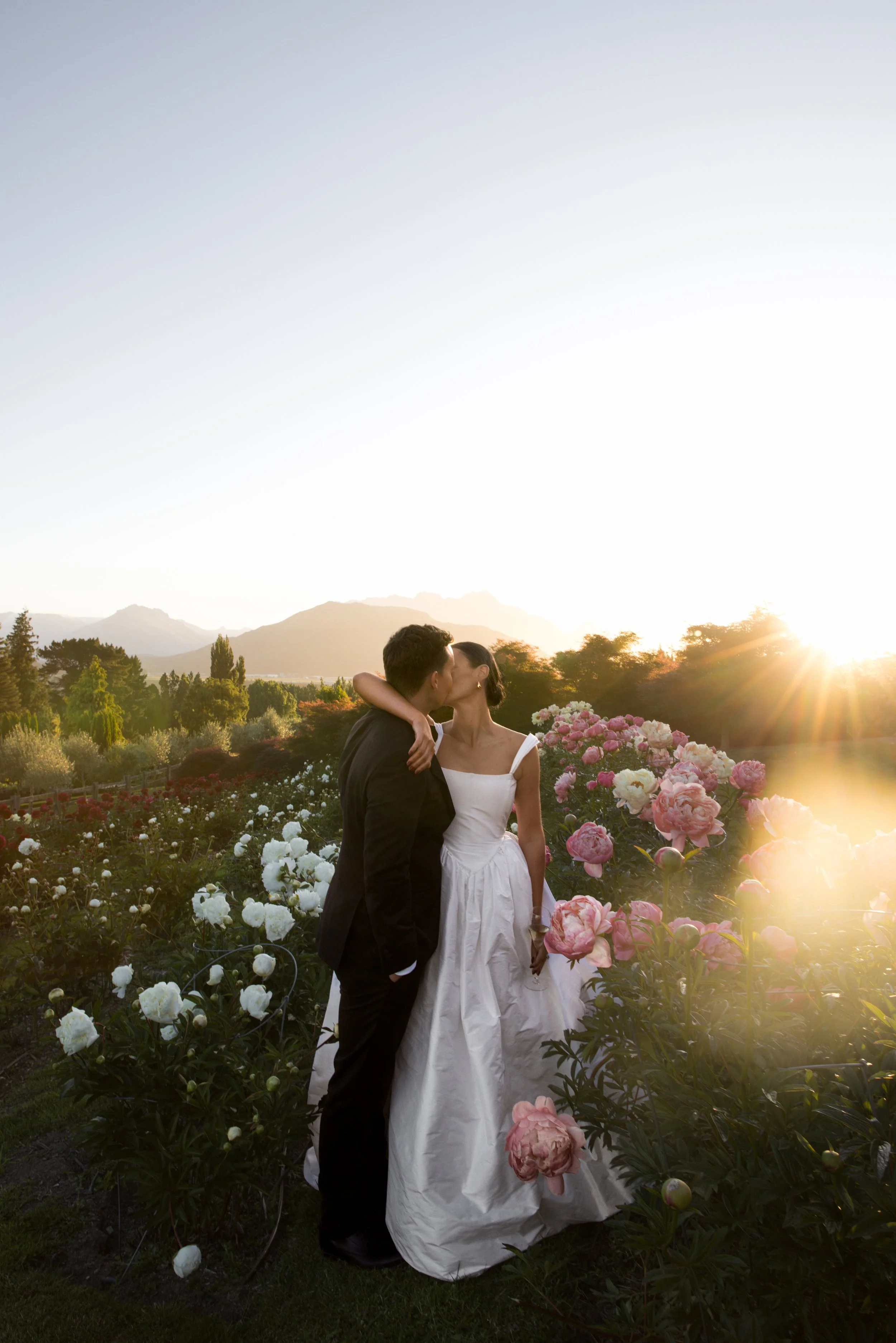 Bride and groom kissing in a field of pink, red and white peonies