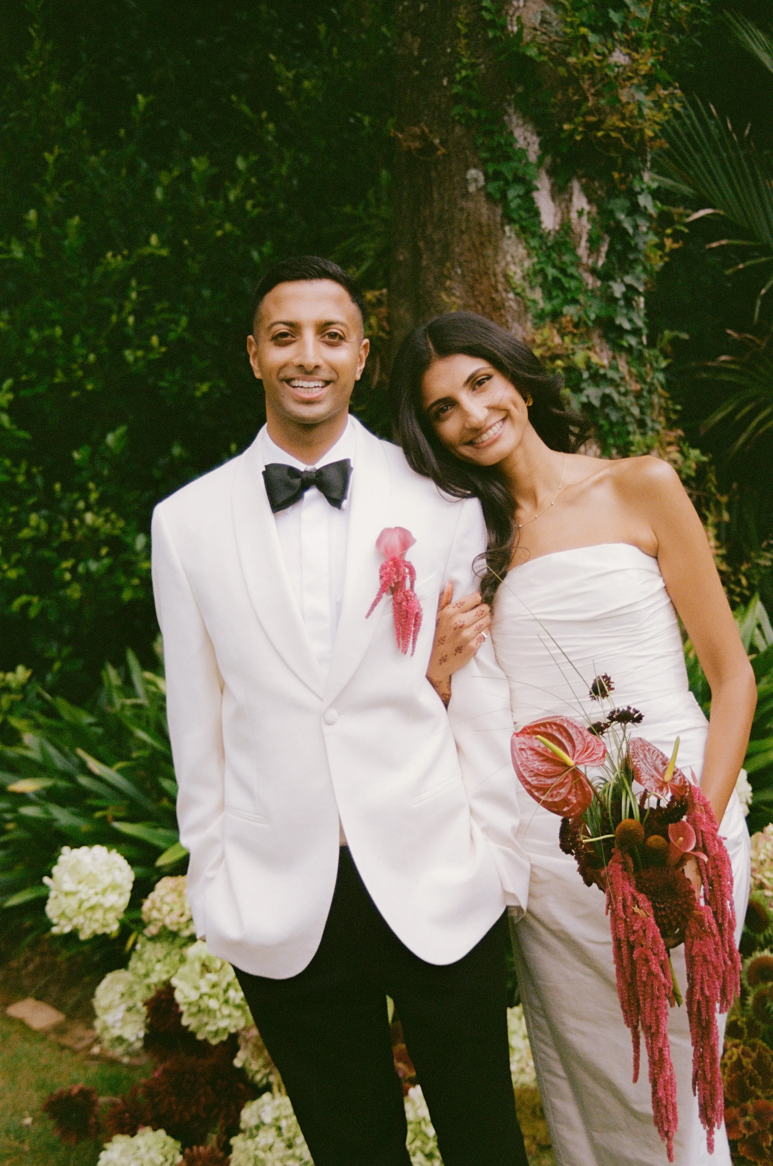 Bride and grrom wearinga buttonhole and holding a bridal bouquets in deep red and burgundy tones