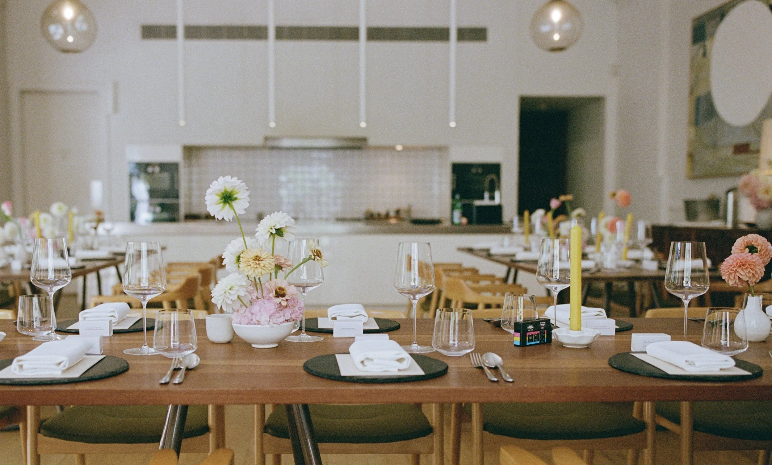 A decorated dining table set with wine glasses, napkins, and floral centerpieces in a bright, modern restaurant or event space.