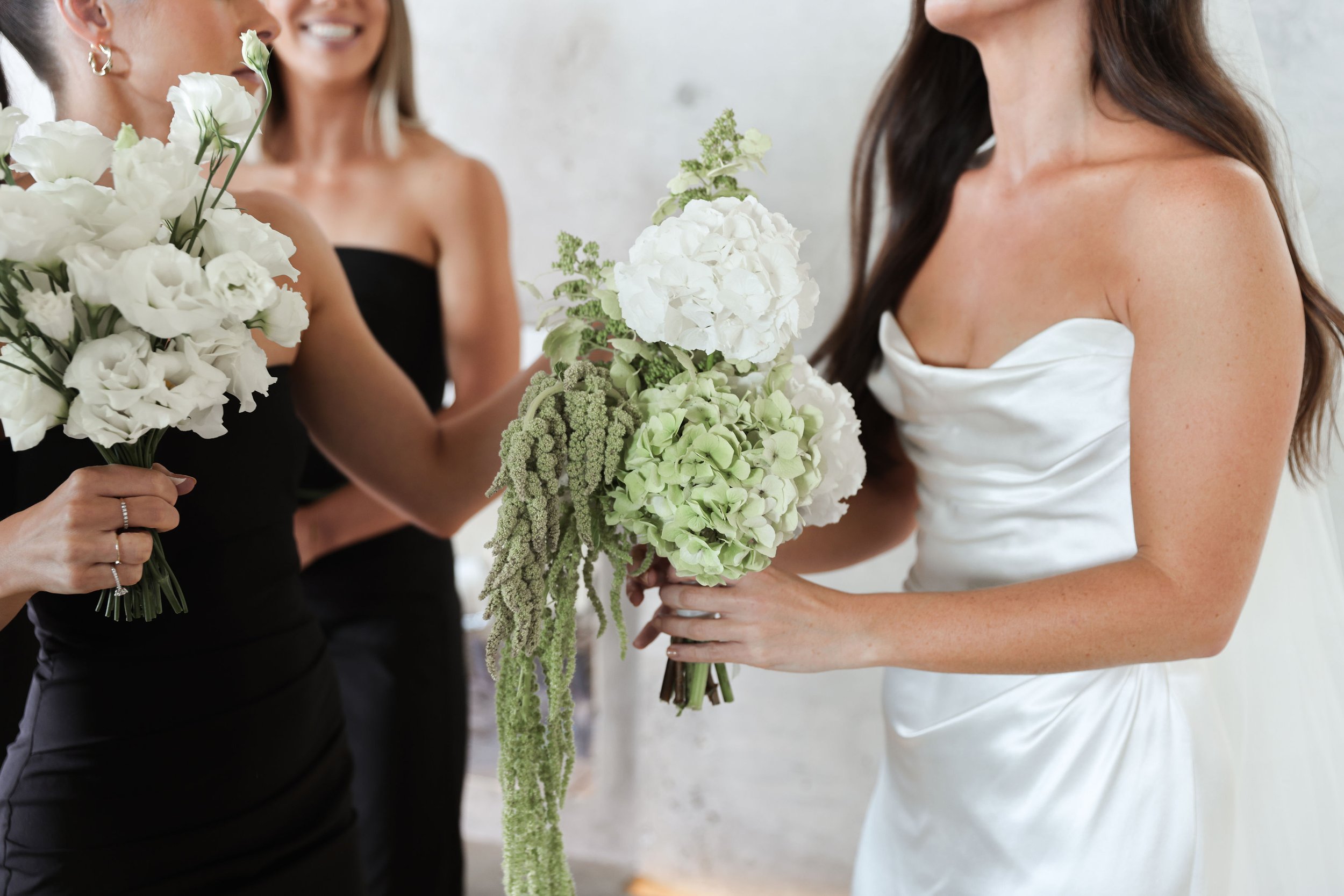 Women in formal dresses exchanging floral bouquets at a wedding celebration.