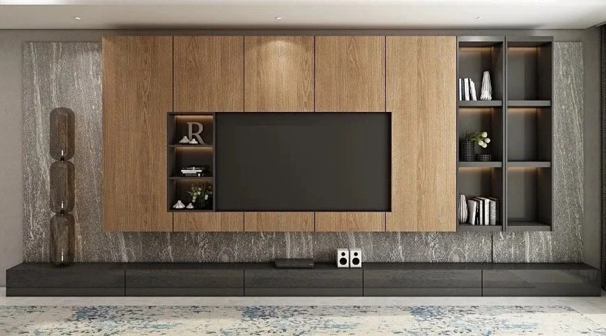 Modern living room entertainment center with a large flat-screen TV mounted on a wooden panel, built-in shelves with decorative items and books, and a long black console underneath, set against a textured gray wall.