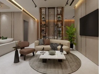 Modern living room with beige walls, a large flat-screen TV, a white sofa, a brown ottoman, and a round rug. There is a glass display cabinet with decorative items and a tall green plant.