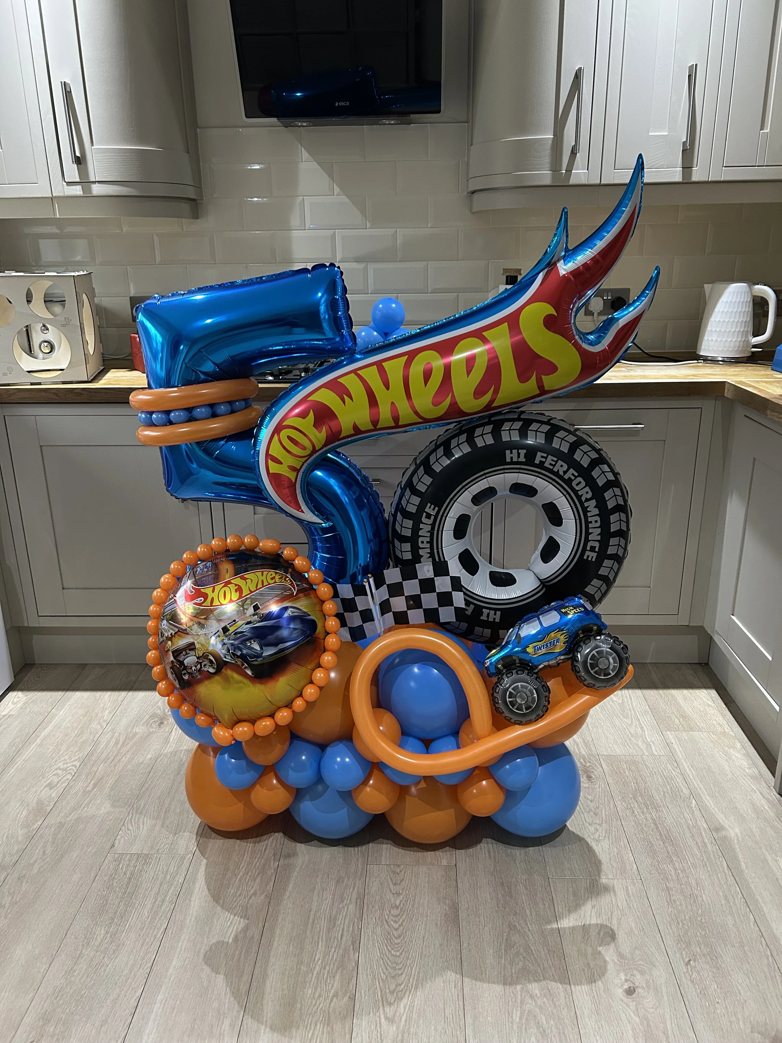 Colorful balloons with Hot Wheels and toy car themes in a kitchen.