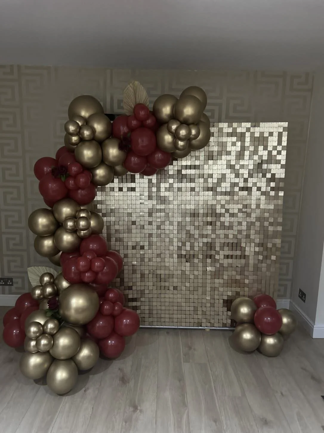 Balloon decoration with gold and red balloons arranged around a shiny mosaic backdrop in a decorated room.