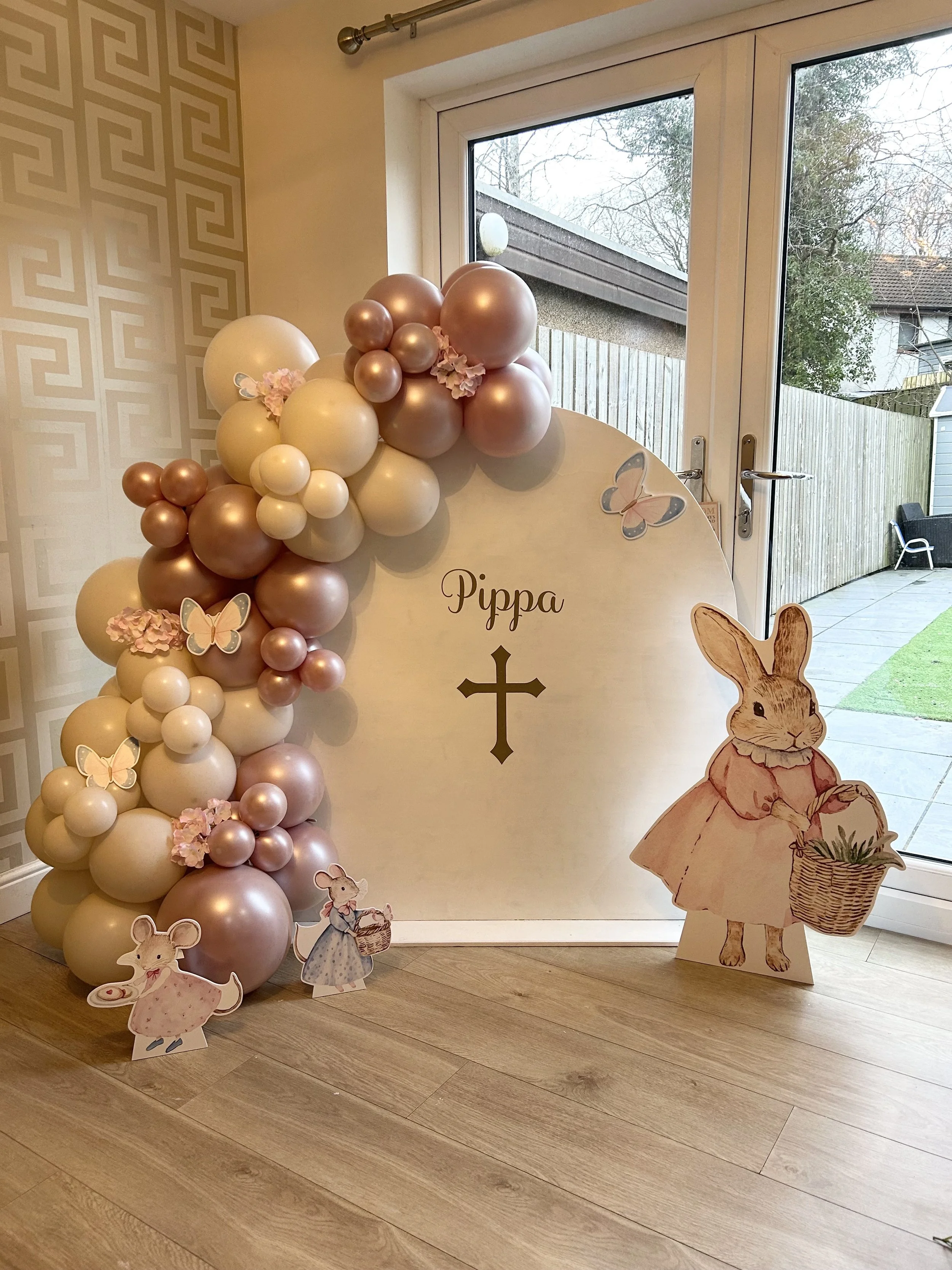 Decorative arrangement of pink, white, and cream balloons along with paper cutouts of anthropomorphic mice and a rabbit. The mice and rabbit are dressed in vintage-style clothing, with the rabbit holding a basket and the mice holding a bow and a cake