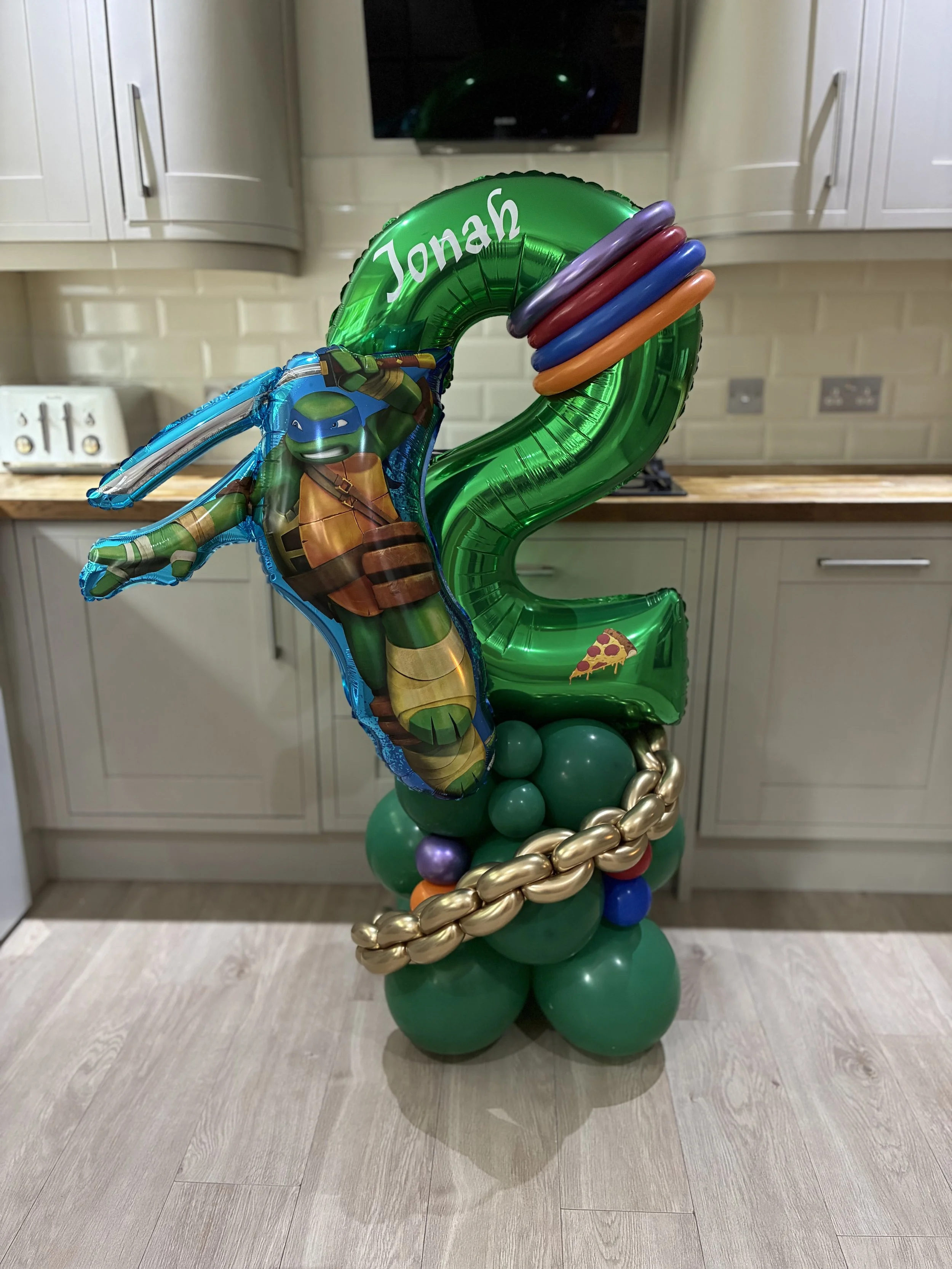 Balloon arrangement with a green number 2, Ninja Turtle figure, and colorful rings.