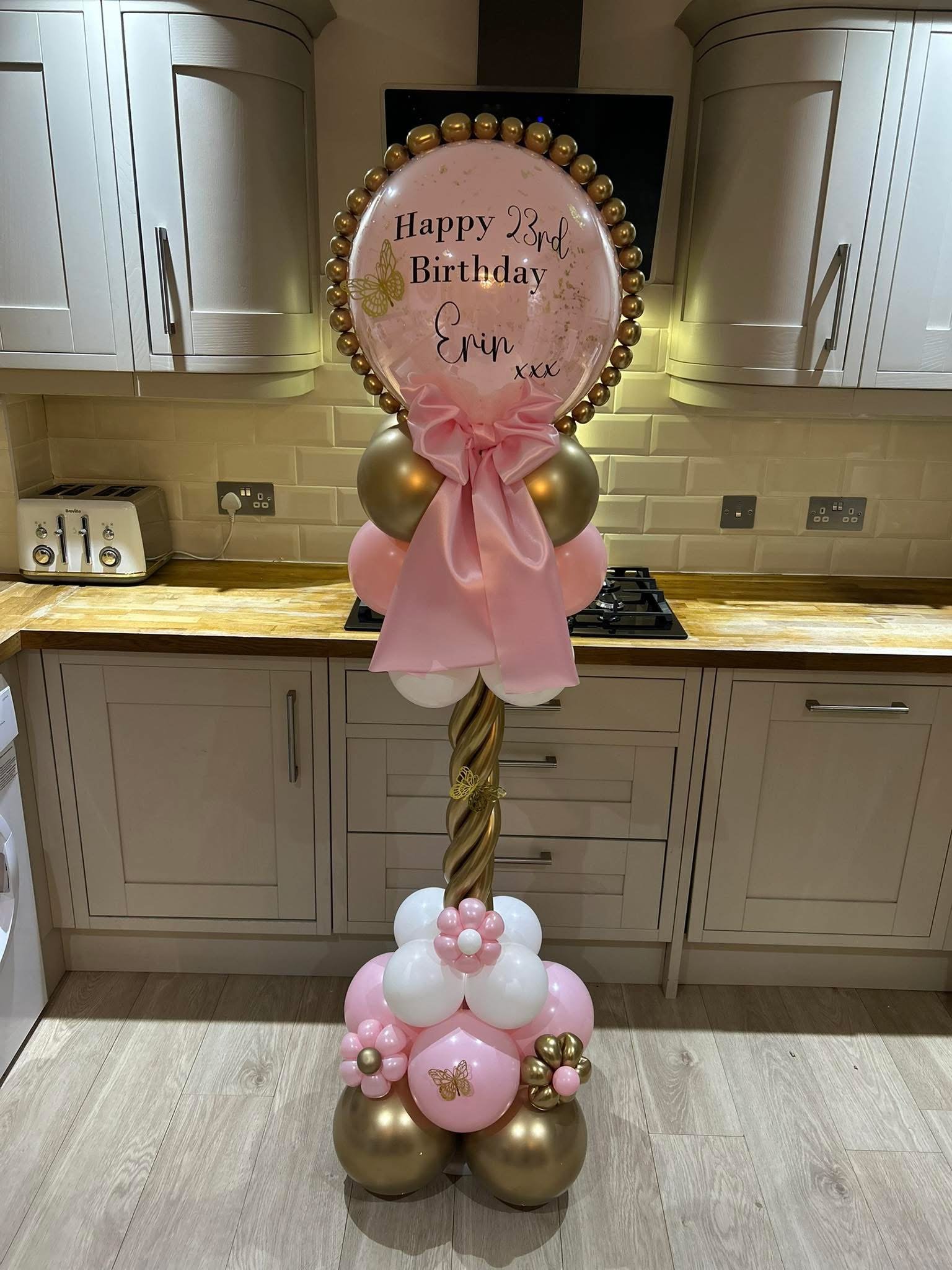 Balloon arch with pink, white, and gold balloons, with a large pink and gold balloon in the center that has a birthday message for Erin's 23rd birthday, decorated with butterfly stickers and a pink ribbon.