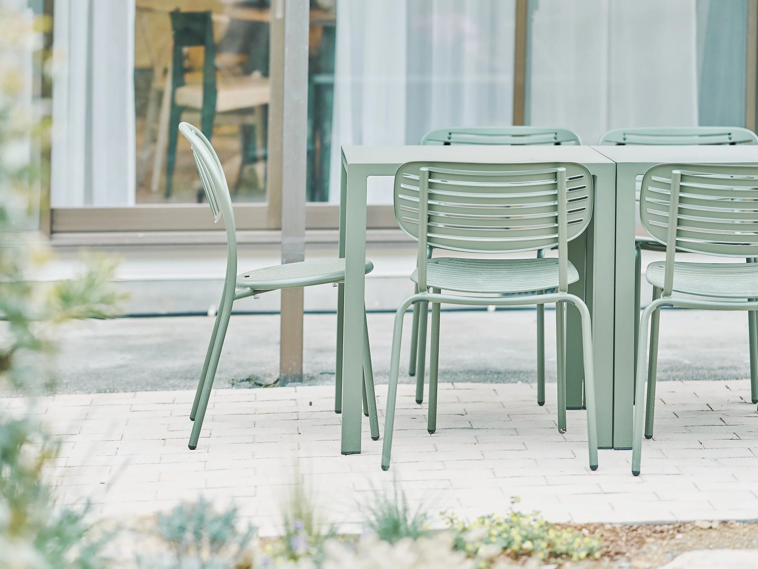 A scene from the outdoor seating area of a café or restaurant, featuring a white table by the window and several white chairs lined up around it