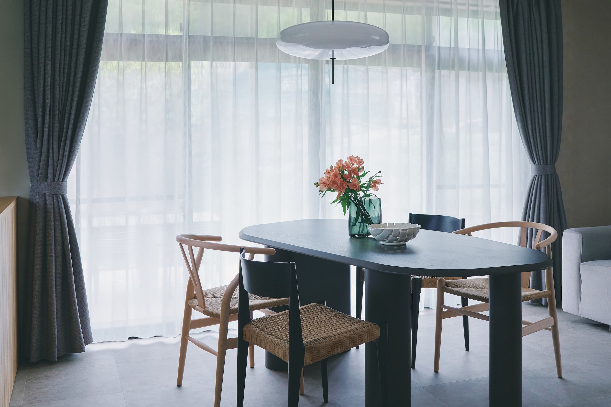 A view of the dining room, with pink flowers in a vase placed in front of the curtains and the table