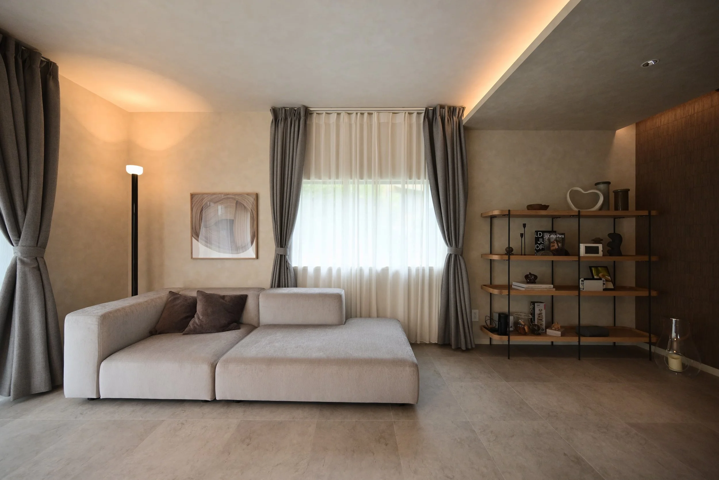 The living room interior features a white sofa, paintings, curtains at the windows, and decorative items, books, and electronic devices on the shelves. The lighting creates a warm atmosphere.