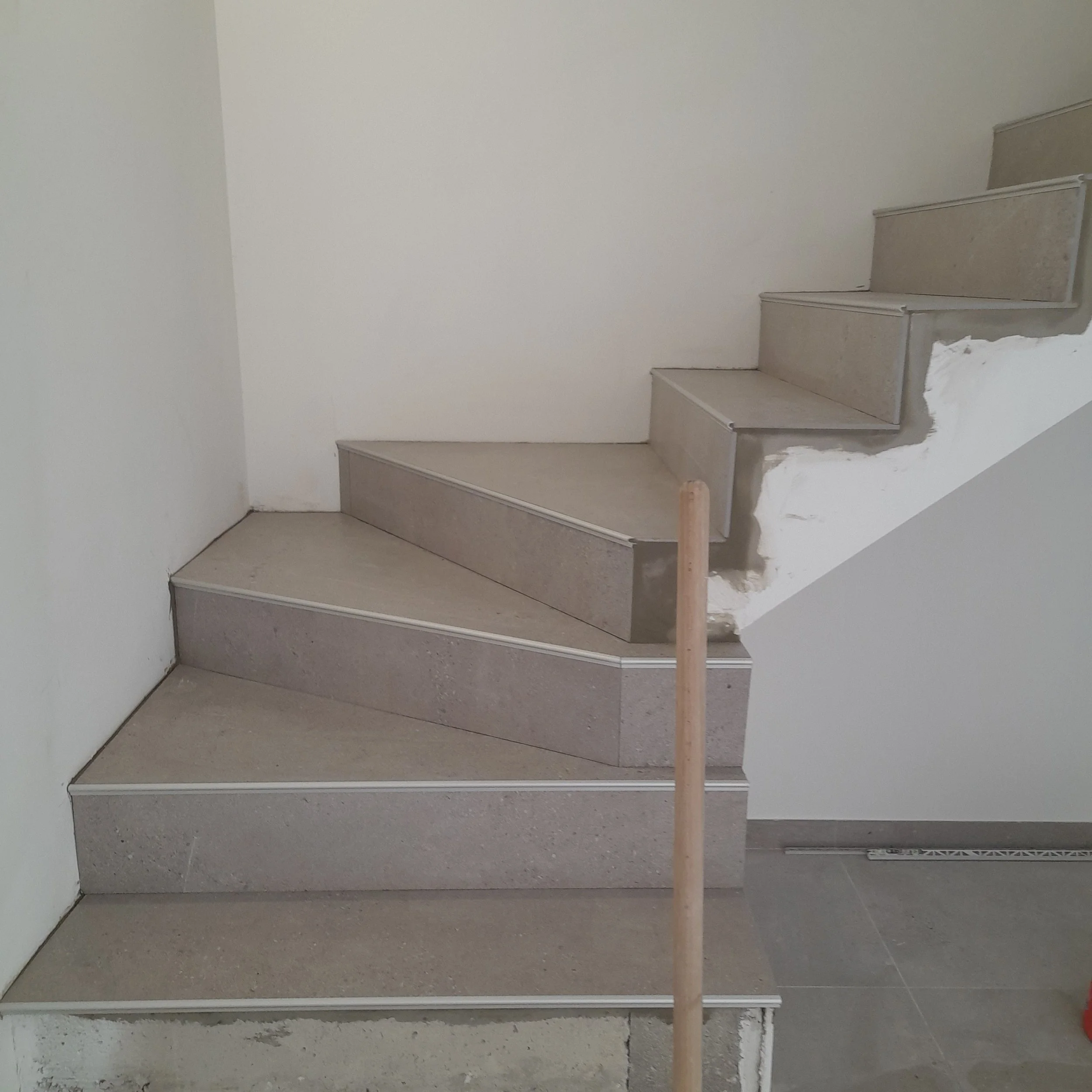 Escalier en cours de construction avec des marches en béton contre un mur blanc, une zone en dessous en travaux.