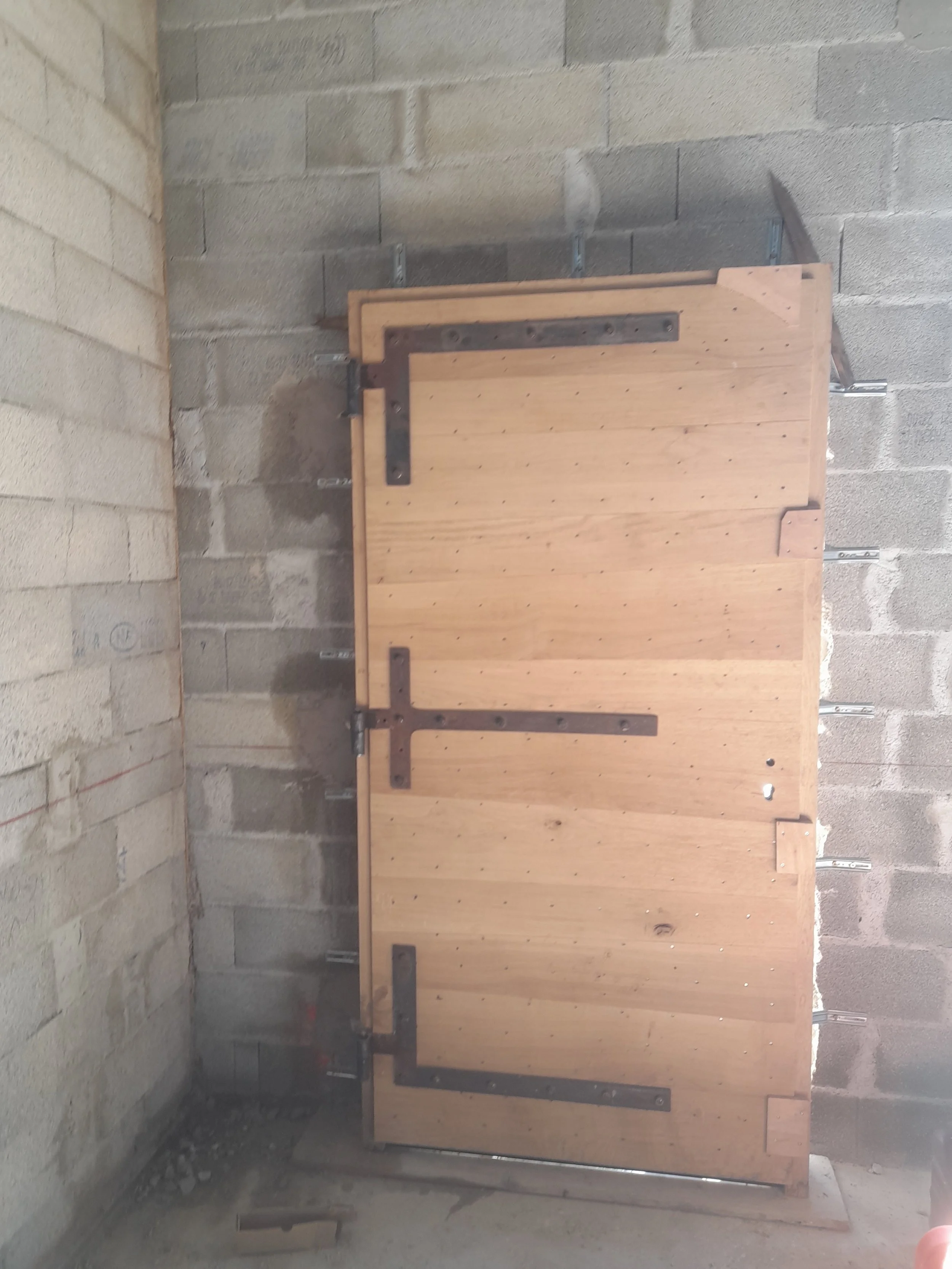Une porte en bois avec des éléments métalliques, installée dans un mur en briques.