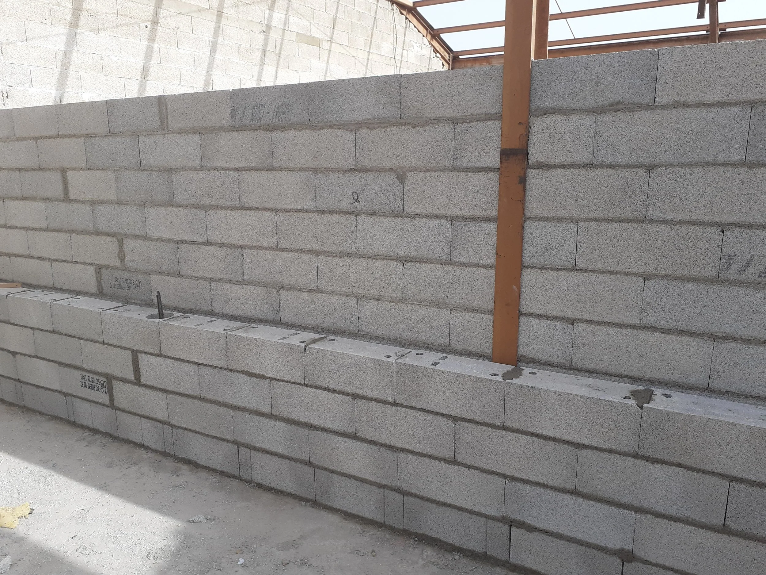 Muret en parpaings de béton en construction avec barres d'acier visibles pour le renforcement.