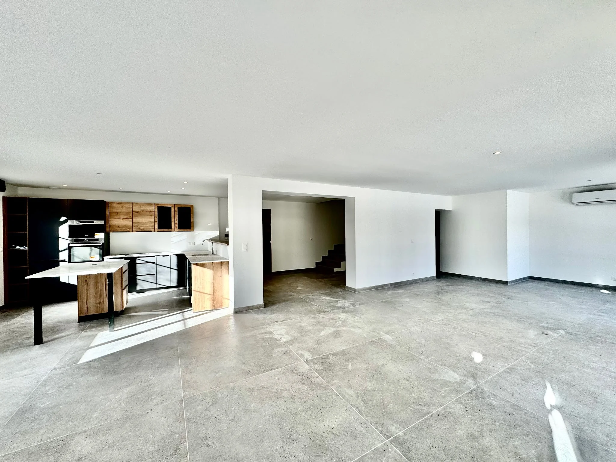 Intérieur moderne avec cuisine en bois et murs blancs, sol en carrelage gris, piéces lumineuses, plafond blanc, escalier en bois, climatiseur mural.