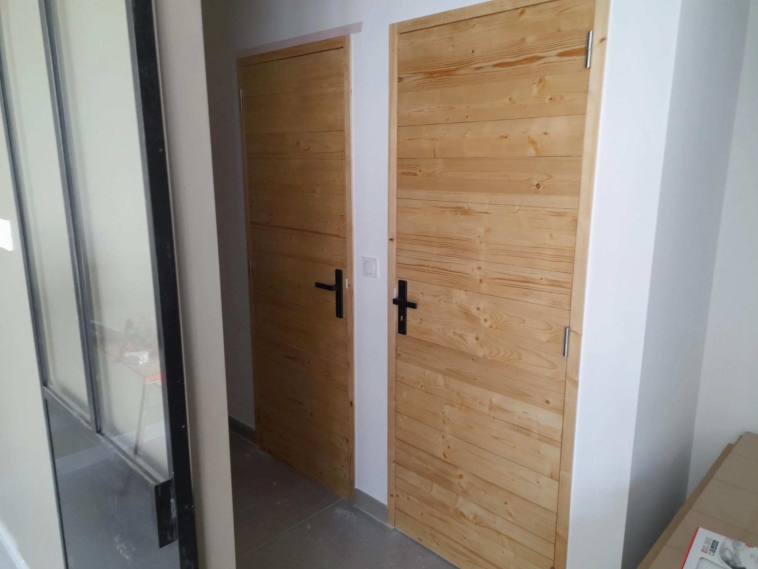 Deux portes en bois naturel avec poignées noires, l'une en bois clair, dans une pièce moderne.