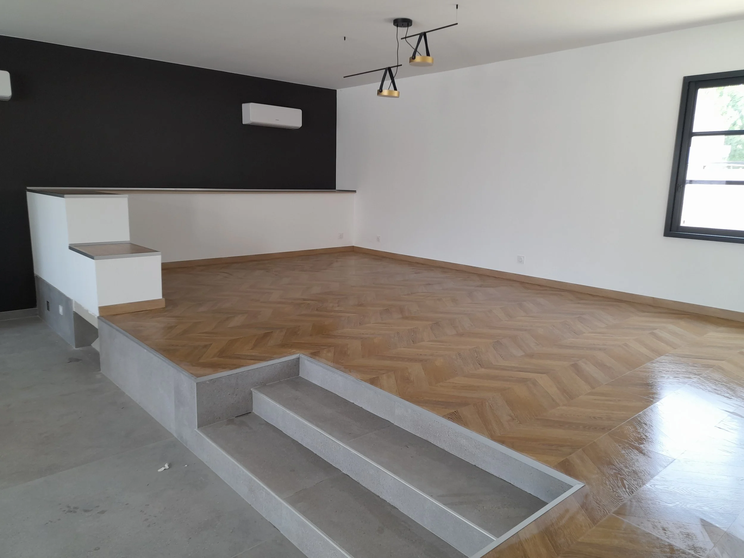 Salon avec plancher en bois clair, mur blanc et mur noir, fenêtre avec vue extérieure, lumière suspendue moderne, ledges en béton surélevées.