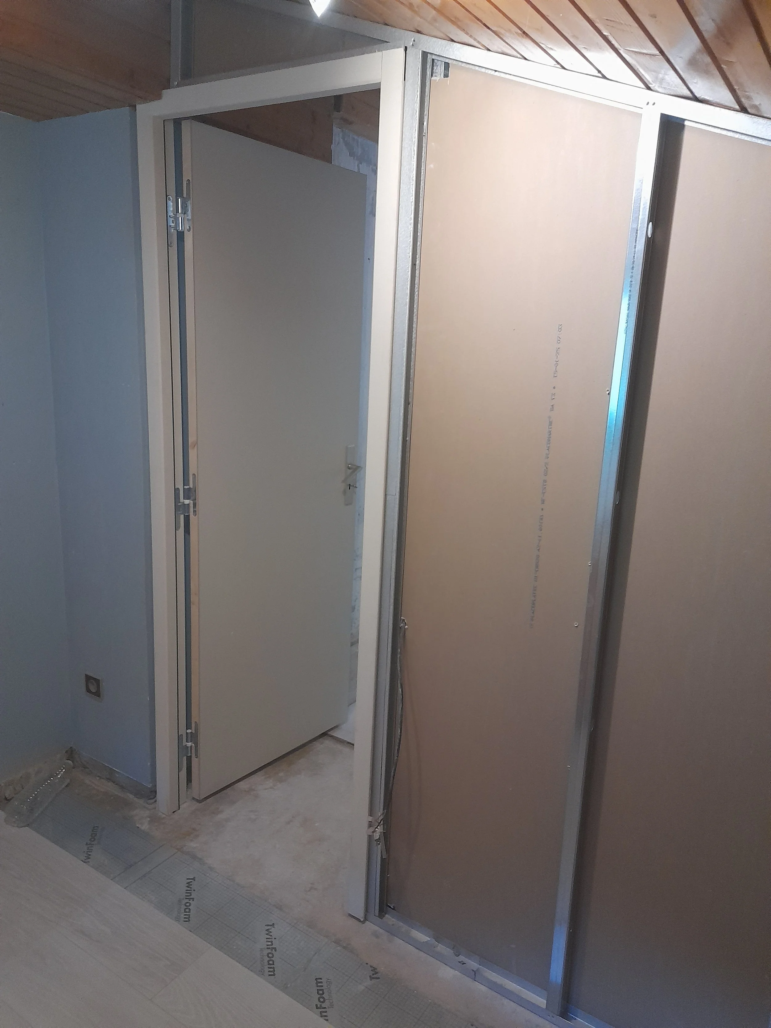 Une cabine de douche en cours d'installation, avec un mur en plaque de plâtre. Sol recouvert de matériau d'étanchéité pour travaux.