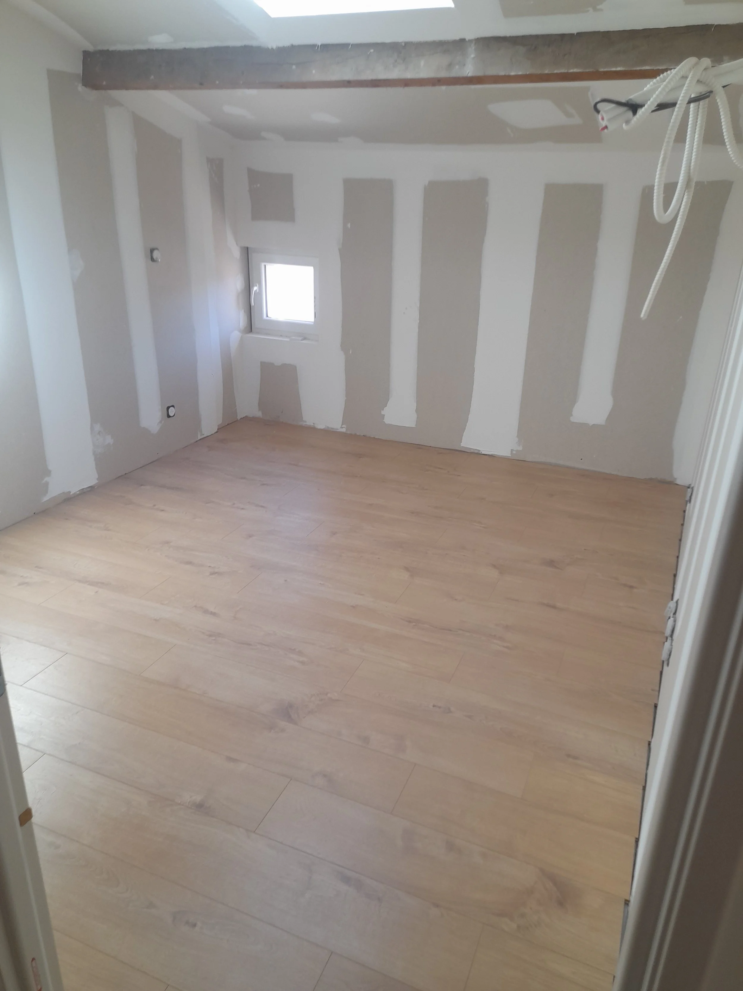 Pièce en cours de rénovation avec murs en drywall et sol en bois clair.