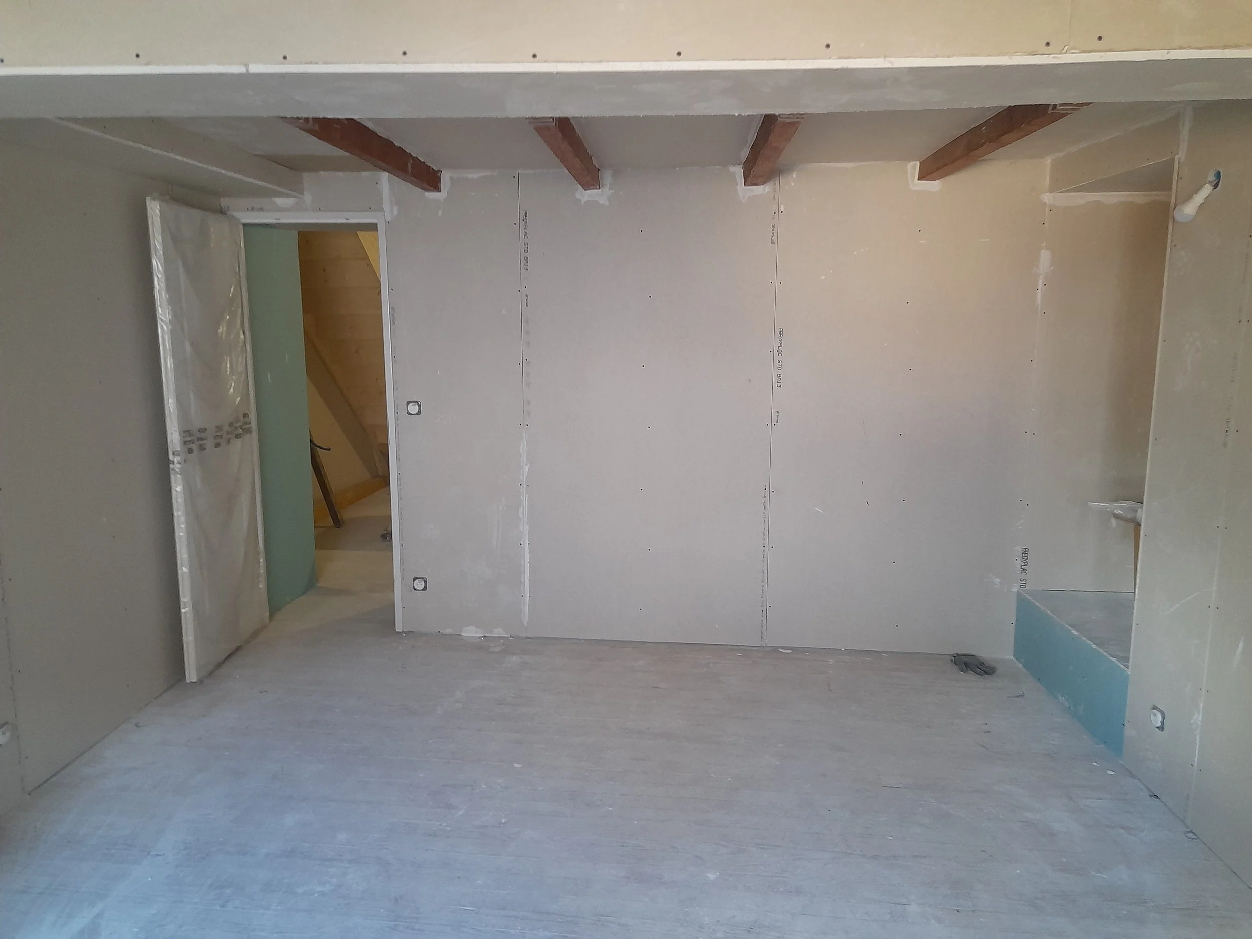 Une pièce en cours de rénovation avec des murs en plaques de plâtre et un plafond en construction, pas de meubles ni de décoration.