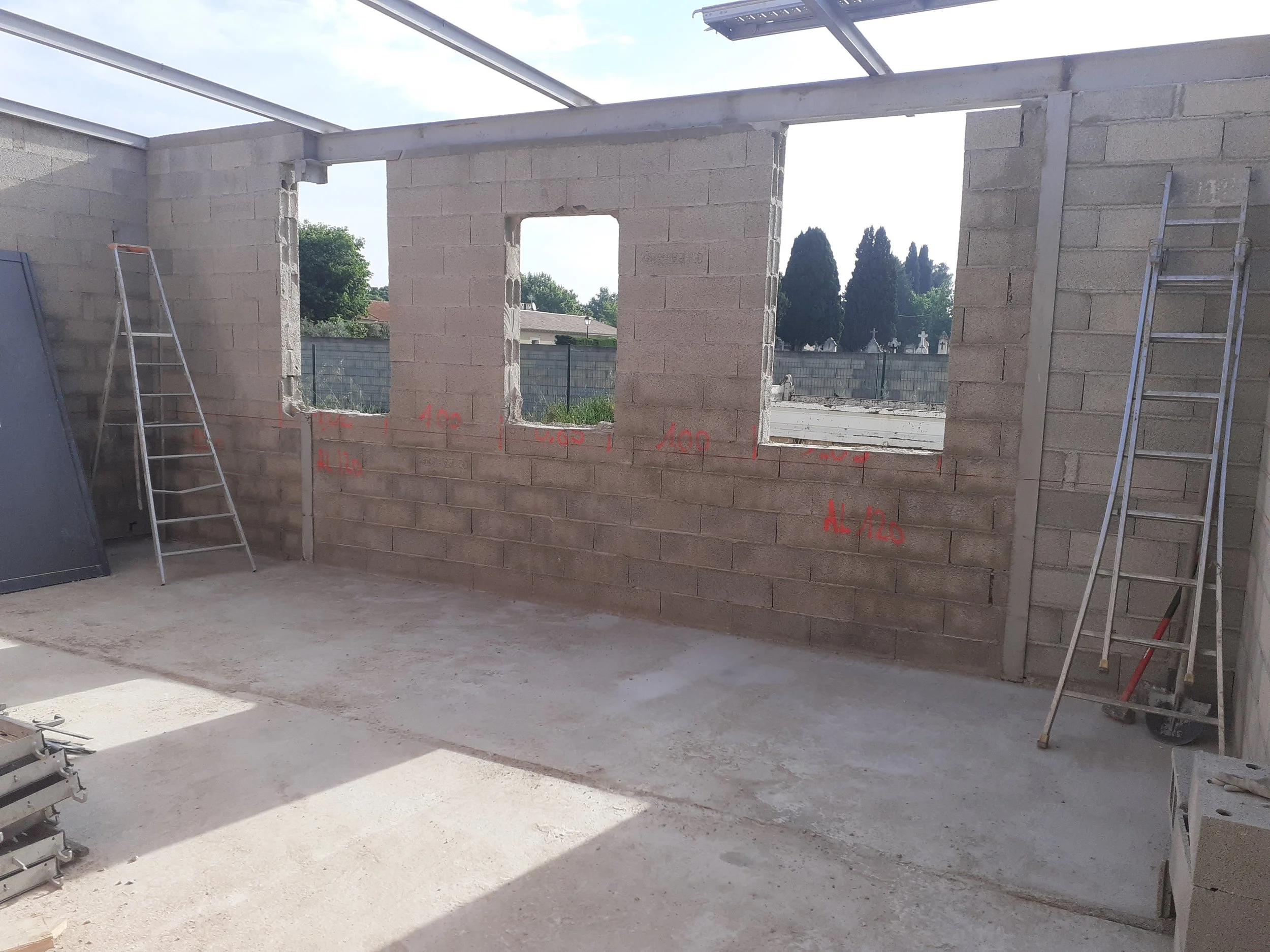 Construction d'une muraille en béton avec fenêtres ouvertures et échelles métalliques dans un site en plein air.