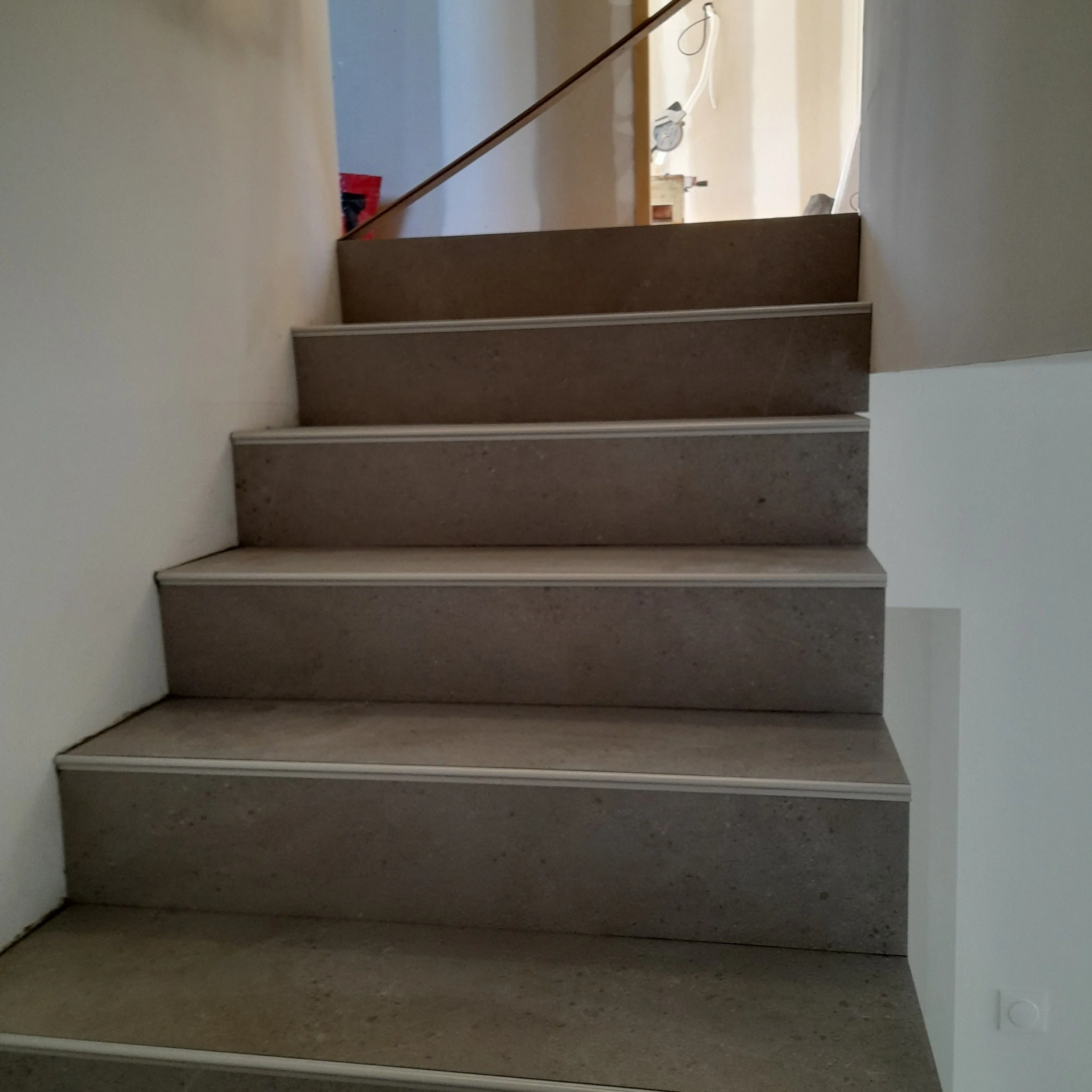 Un escalier en bois dans une maison, vue d'en haut avec un mur blanc sur le côté.