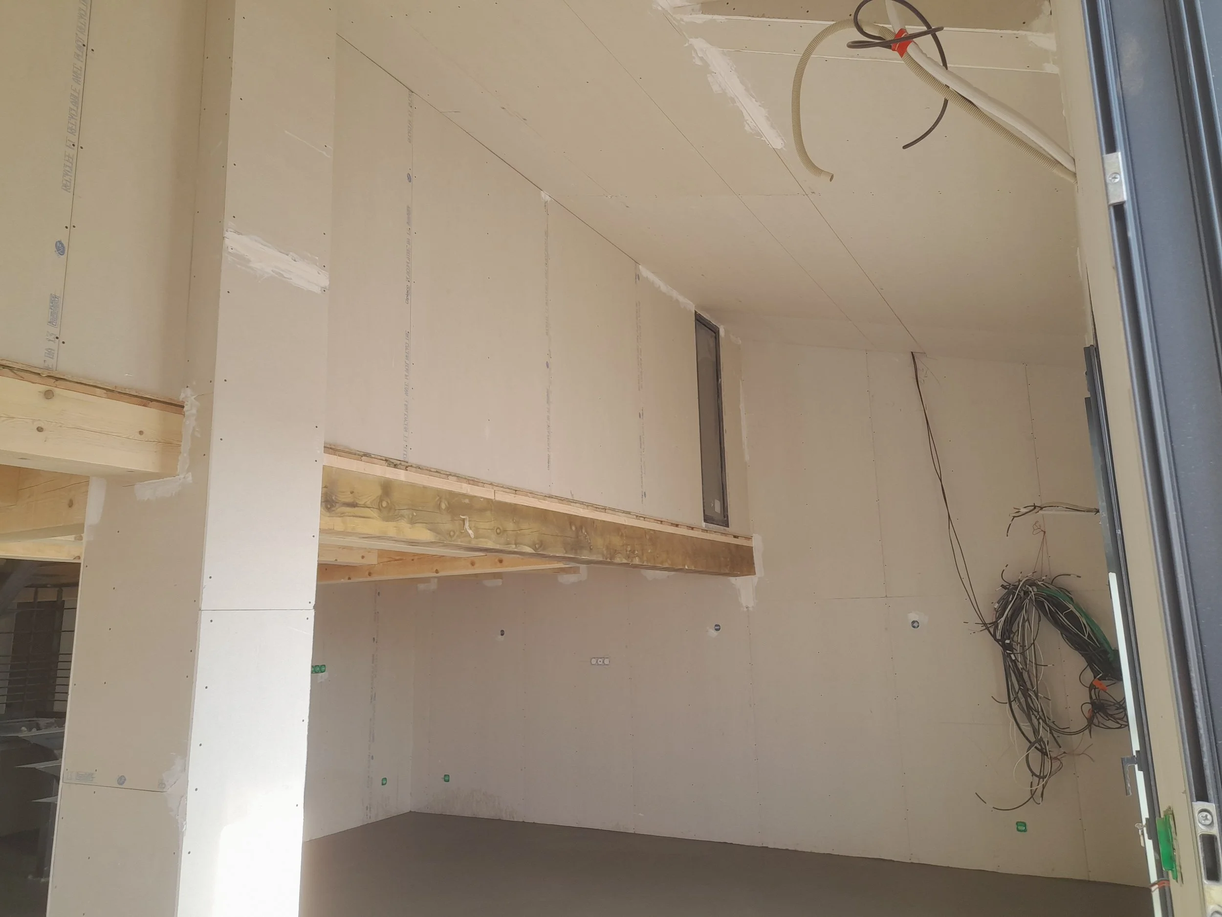 Une pièce en cours de construction avec des murs en placoplâtre, des câbles électriques, et un sol en train d'être préparé.