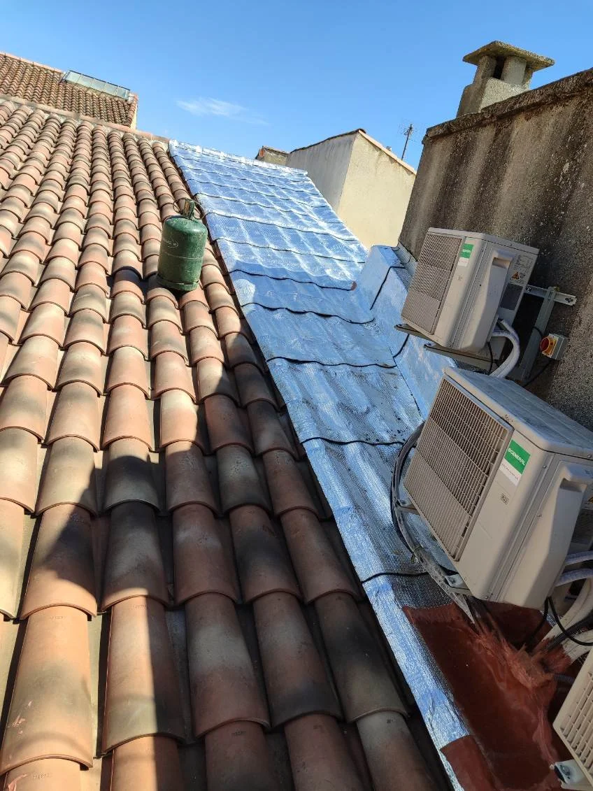 Toit de maison avec tuiles en terre cuite, moitié rénovée avec membrane réfléchissante, et deux unités de climatisation à l'extérieur.
