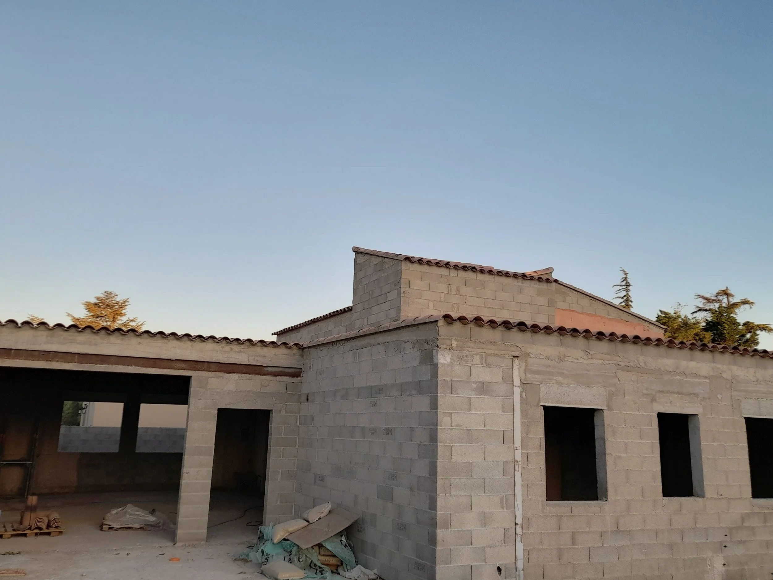Construction d'une maison en briques avec un toit en tuiles, sous un ciel clair.
