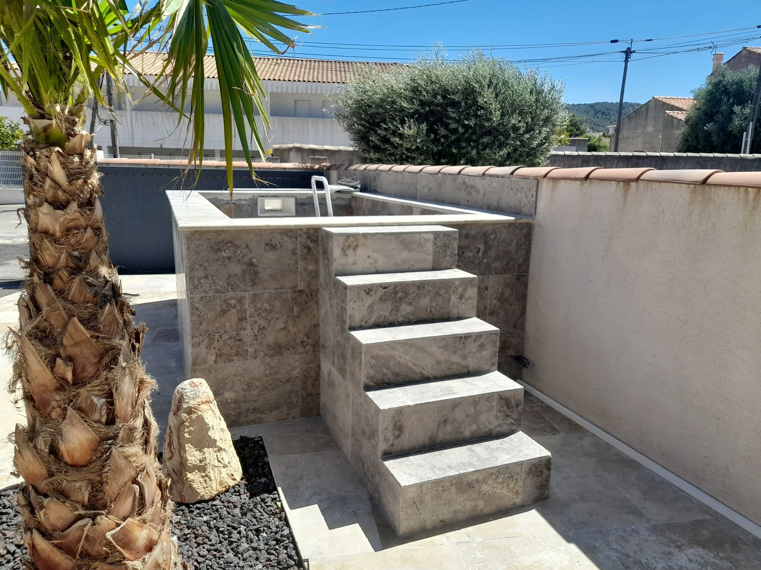 Escalier en pierres menant à une terrasse extérieure avec un mur en béton et des arbres en arrière-plan.