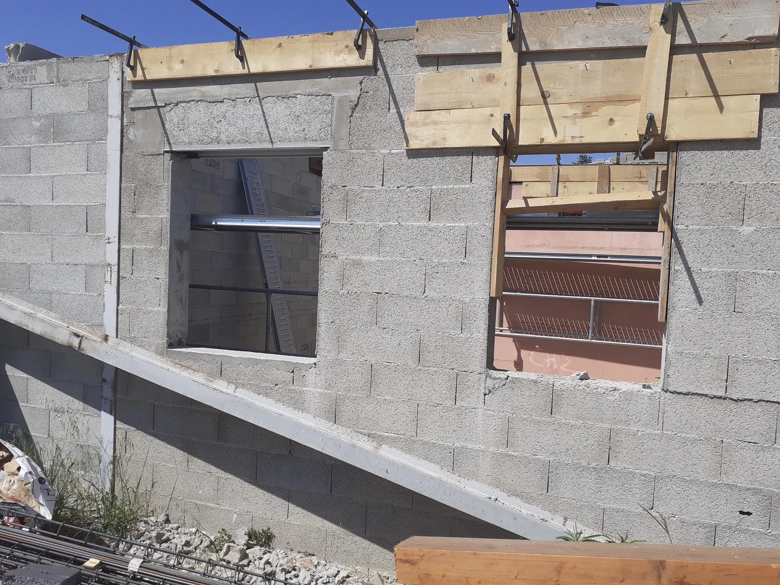 Construction de mur en parpaings avec encadrements de fenêtres en cours, quelques outils et matériaux visibles.