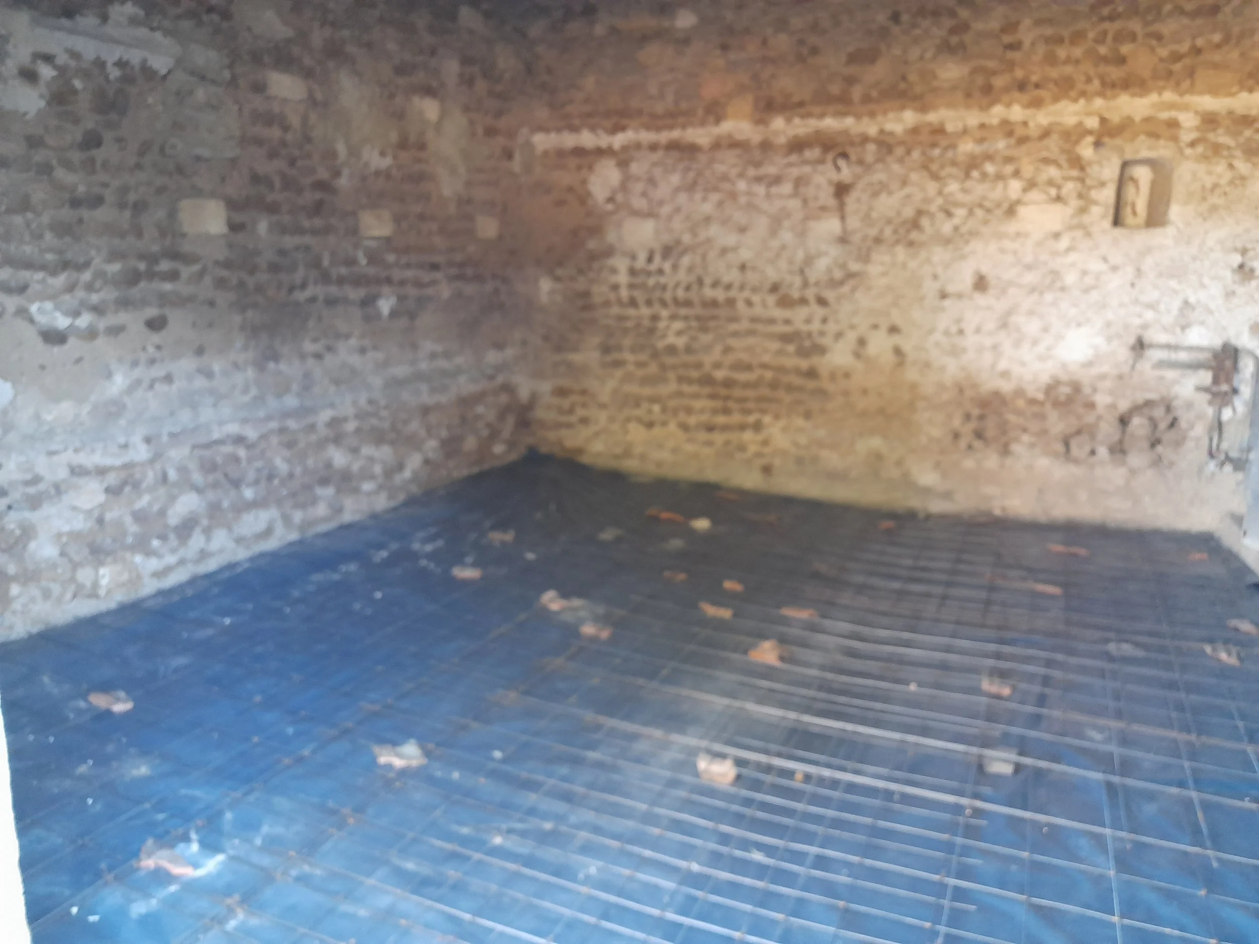 Une salle avec un mur en briques apparentes, un sol en bois foncé, et un projecteur suspendu au plafond.
