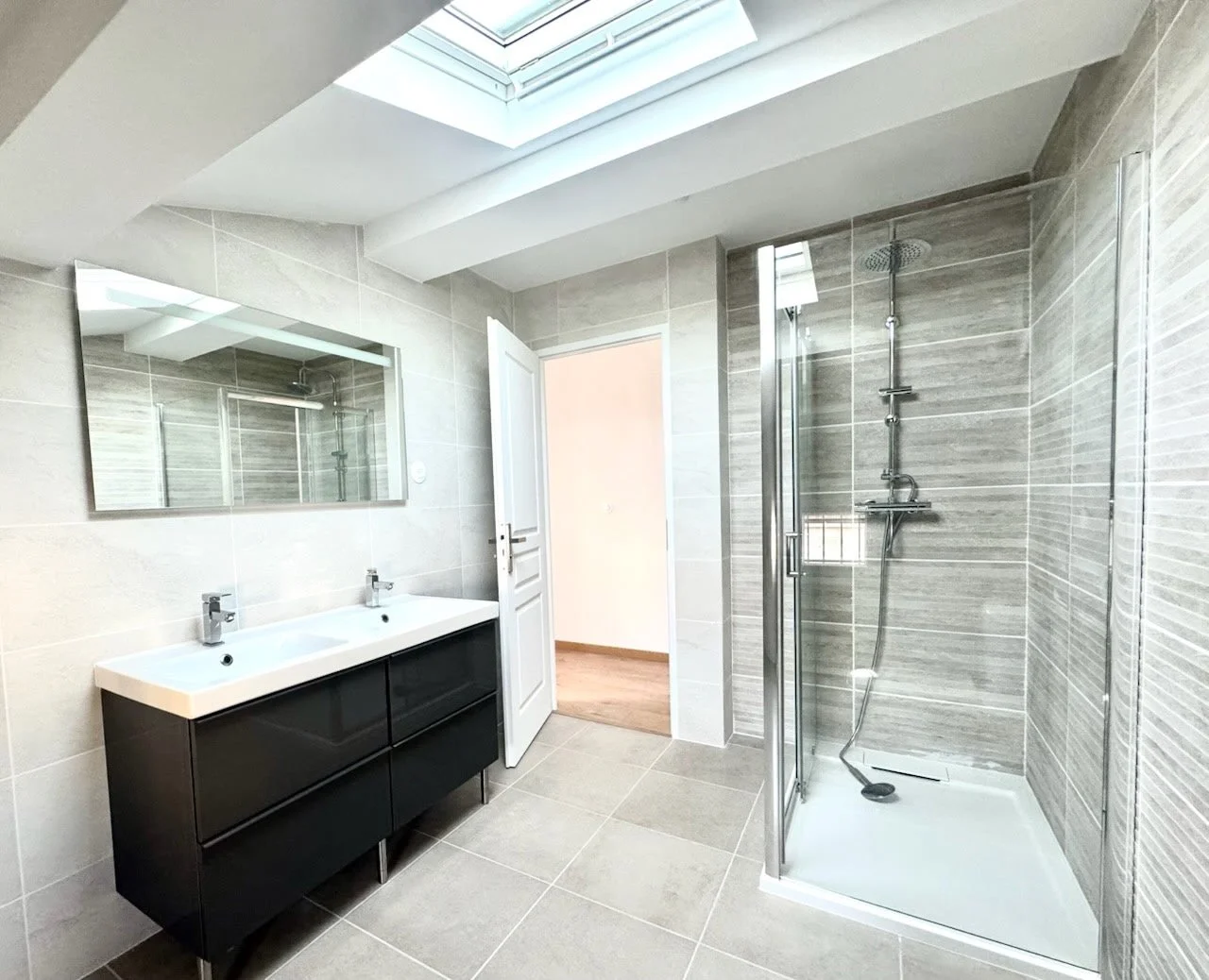 Salle de bain moderne avec double lavabo, grand miroir, douche à l'italienne et fenêtre de toit pour la lumière naturelle
