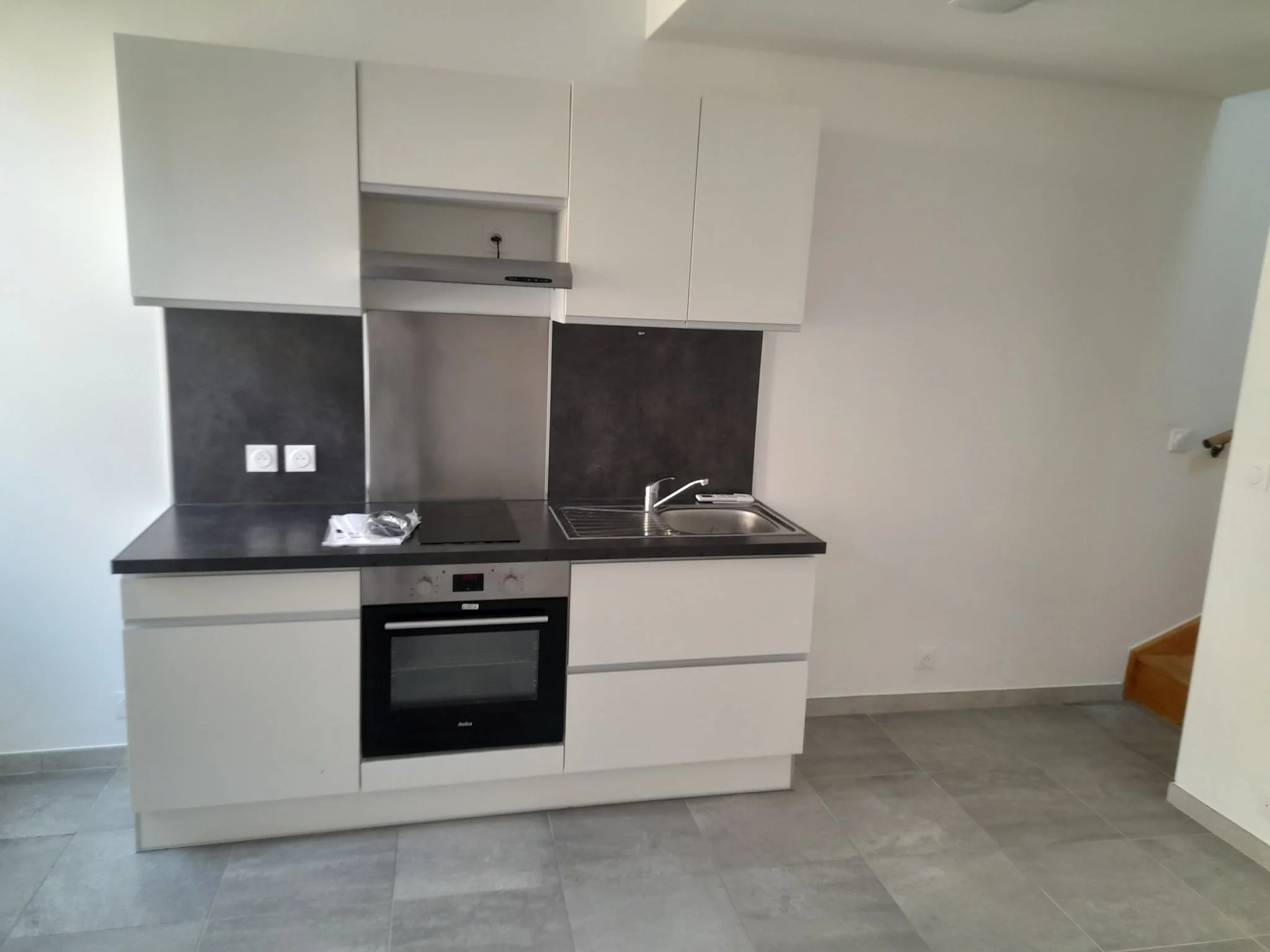 Cuisine moderne avec four, plaque de cuisson, évier et armoires blanc, sol en carreaux gris.