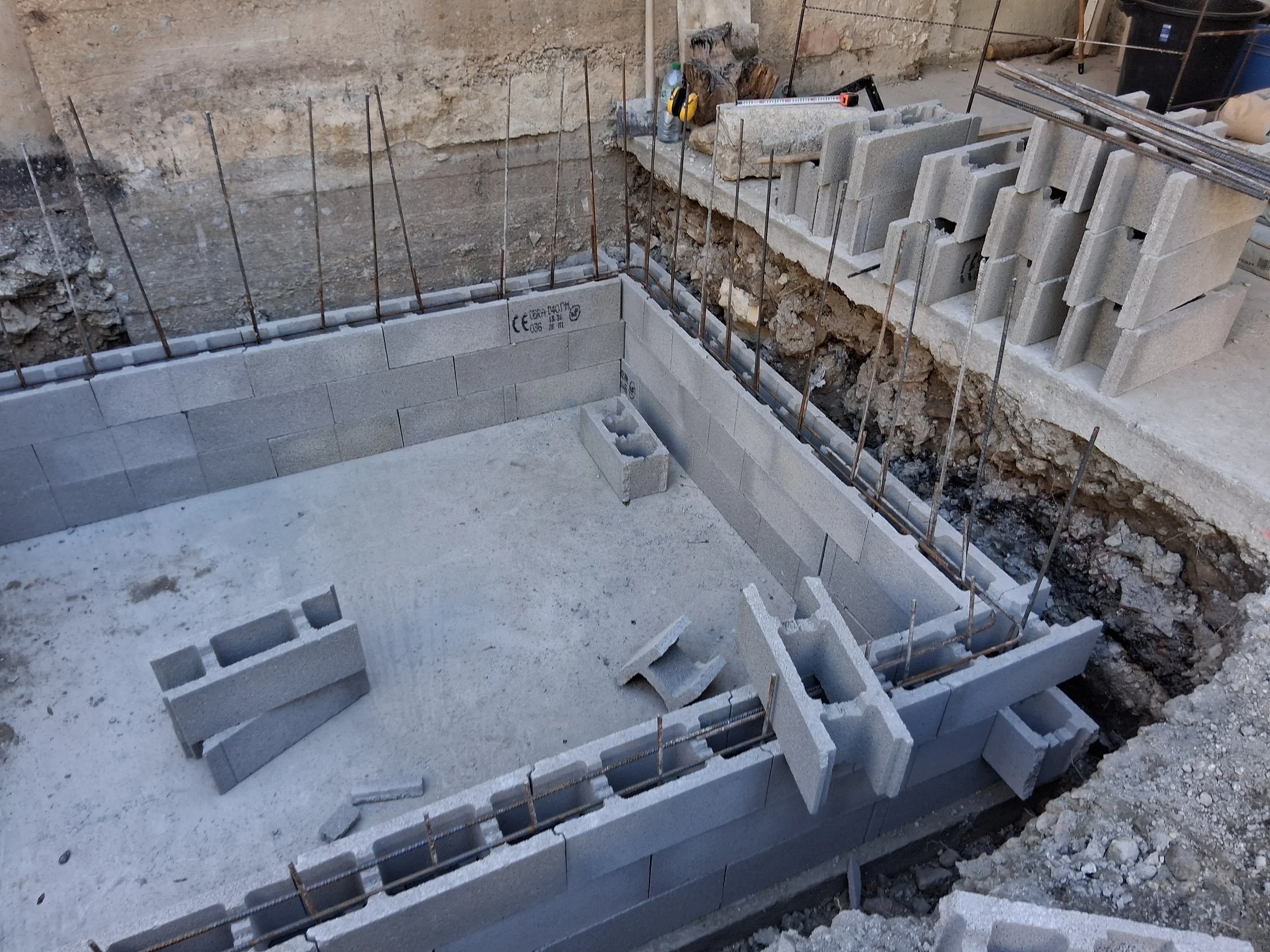 Travaux de construction avec des blocs de béton empilés et des barres d'armature métalliques, dans un espace en excavation