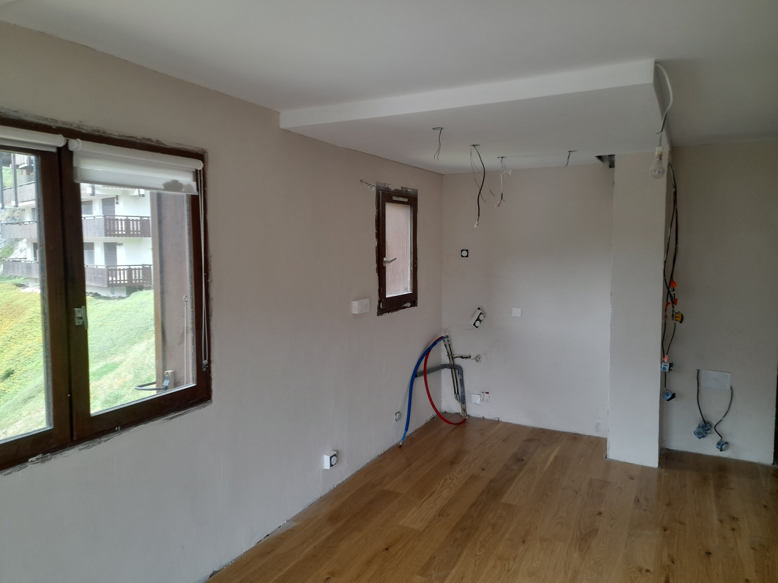 Pièce en rénovation avec fils électriques suspendus au plafond, fenêtres et parquet en bois.