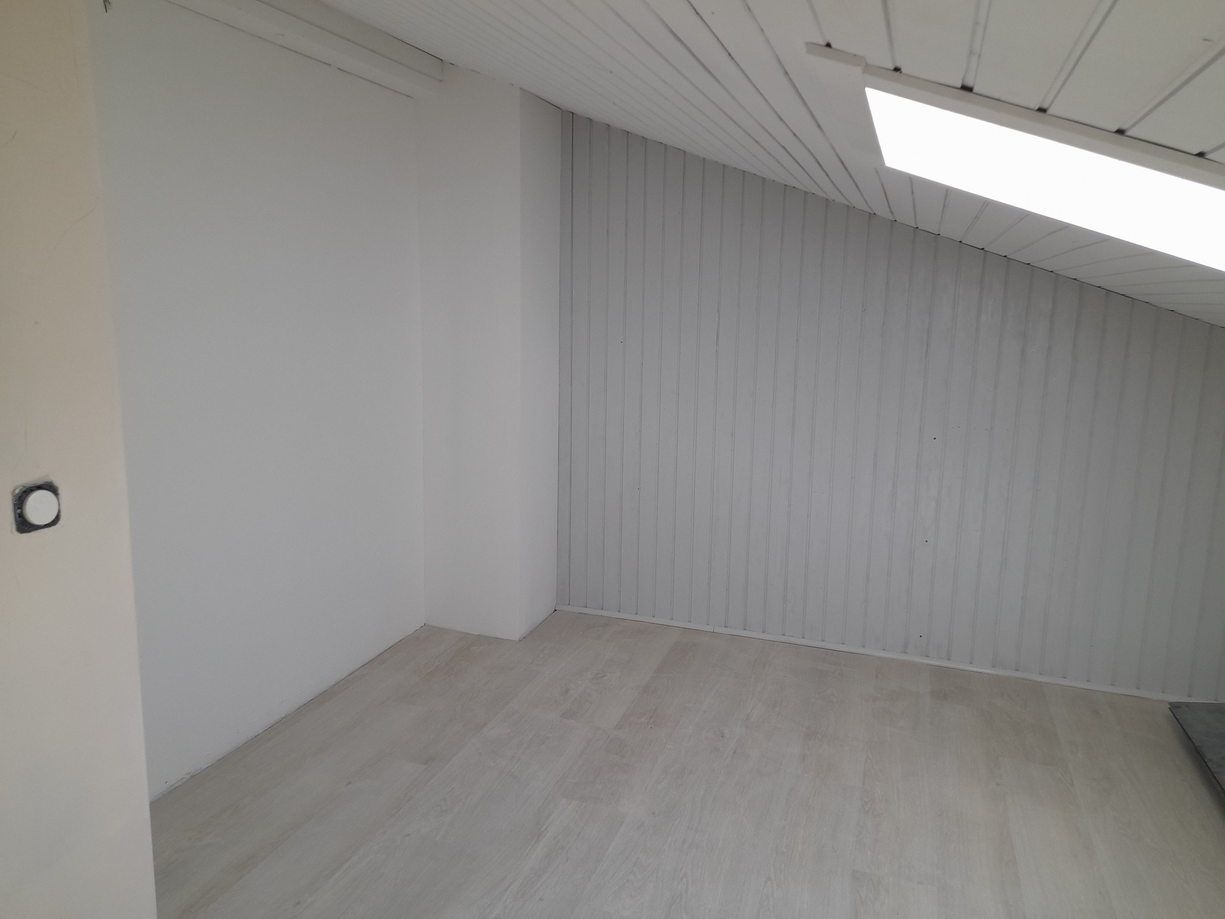Une pièce vide avec des murs et un plafond blancs, un carrelage gris clair et un conduit d'air sur le mur.