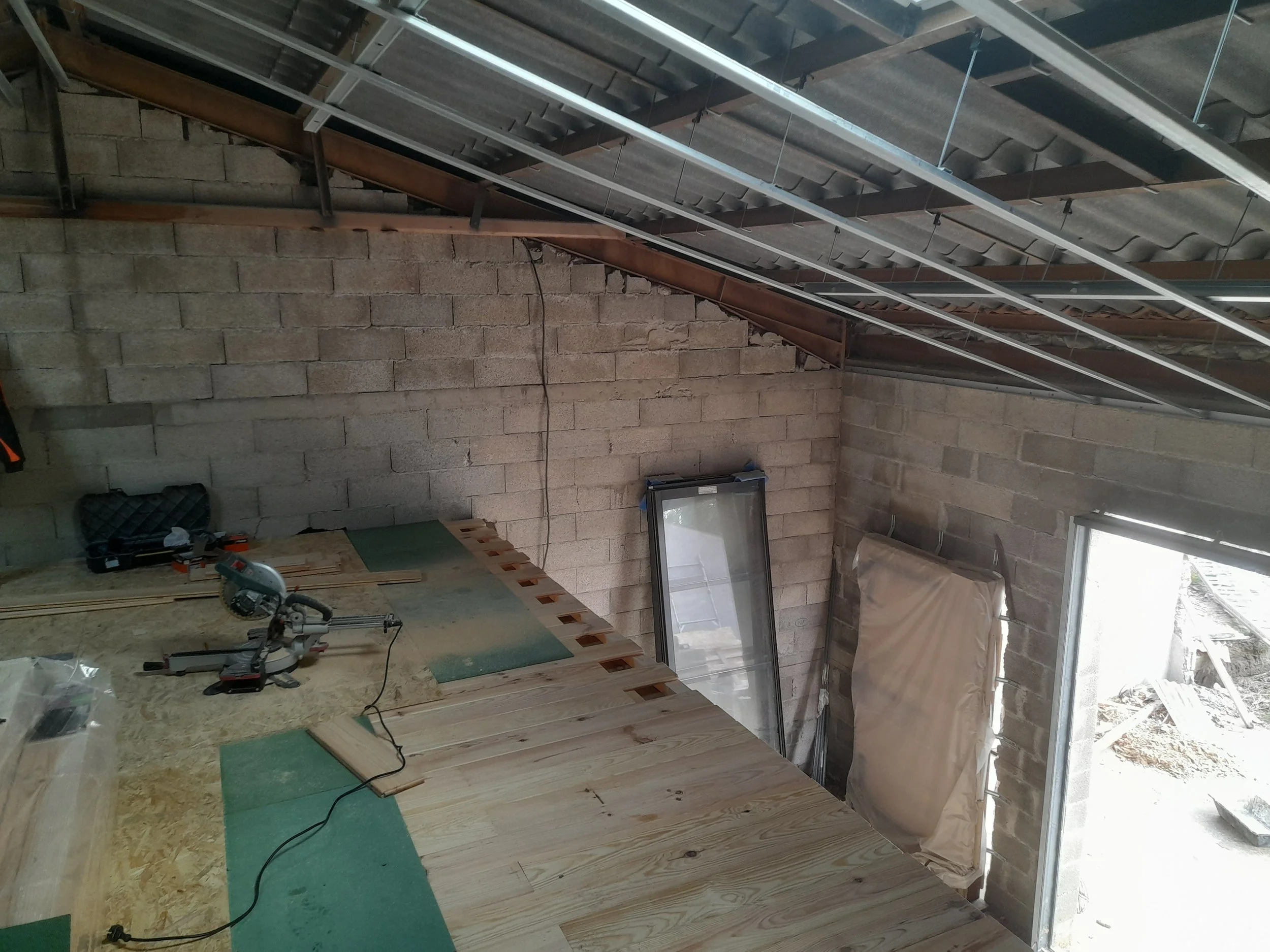 Les travaux de construction dans un intérieur partiellement terminé, avec des murs en briques, un sol en bois, et des matériaux de construction, y compris une scie électrique et d'autres outils.