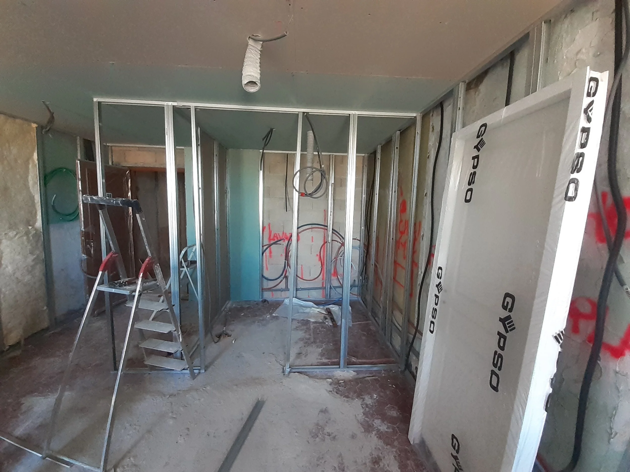 Construction intérieure en cours avec cadres métalliques pour murs, câblage électrique visible et escabeau en place.