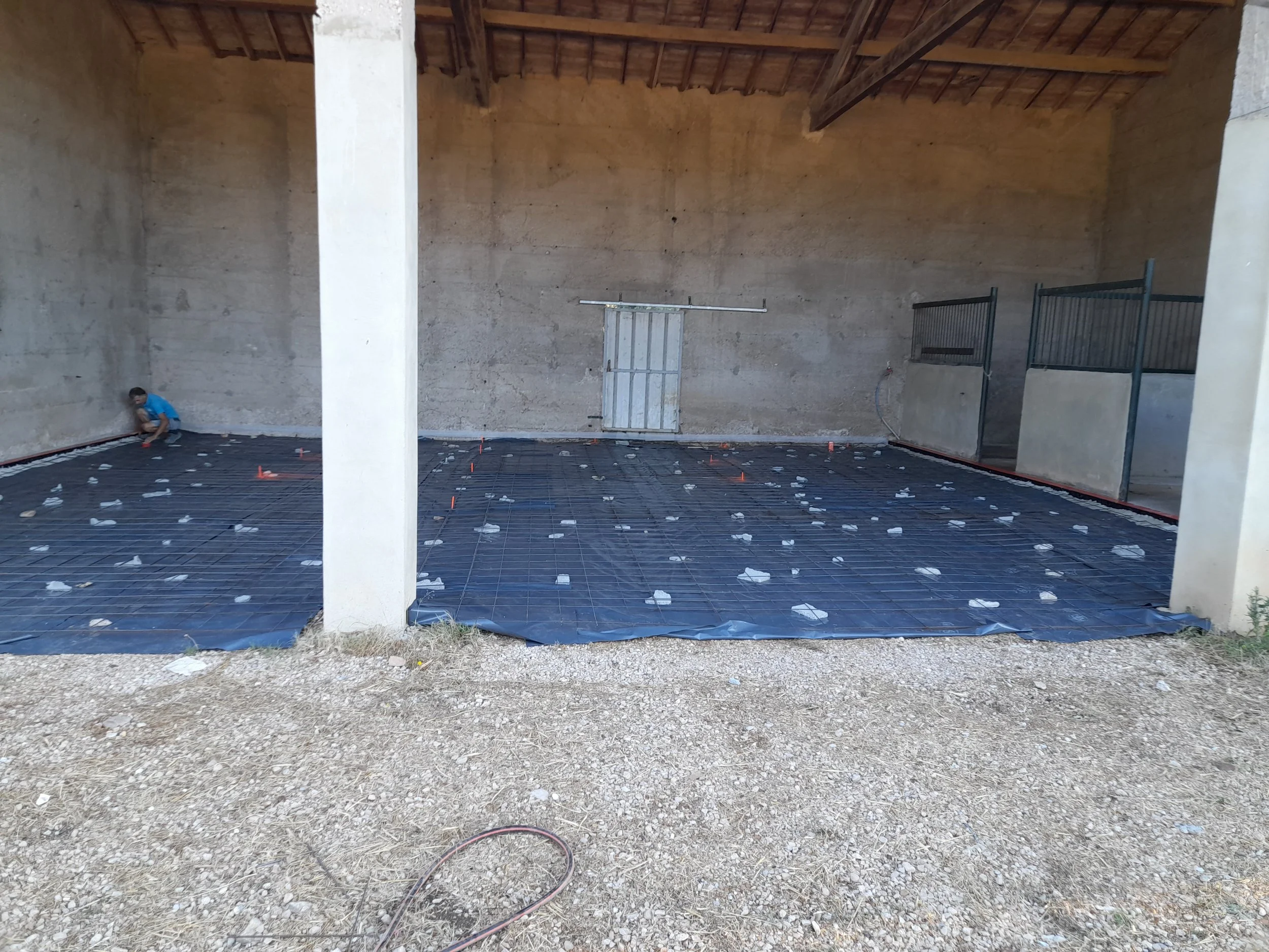 Construction d'une salle intérieure avec une dalle en béton armé au sol, une petite porte en métal blanc à l'arrière, et des barres d'armature métalliques disposées pour le coulage du béton.