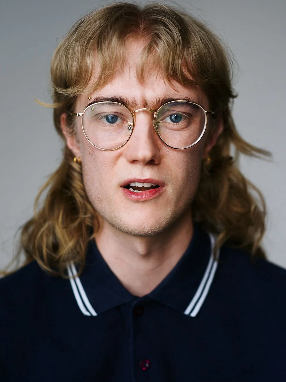 Portrait of young person with glasses and curly hair, casual polo shirt headshot