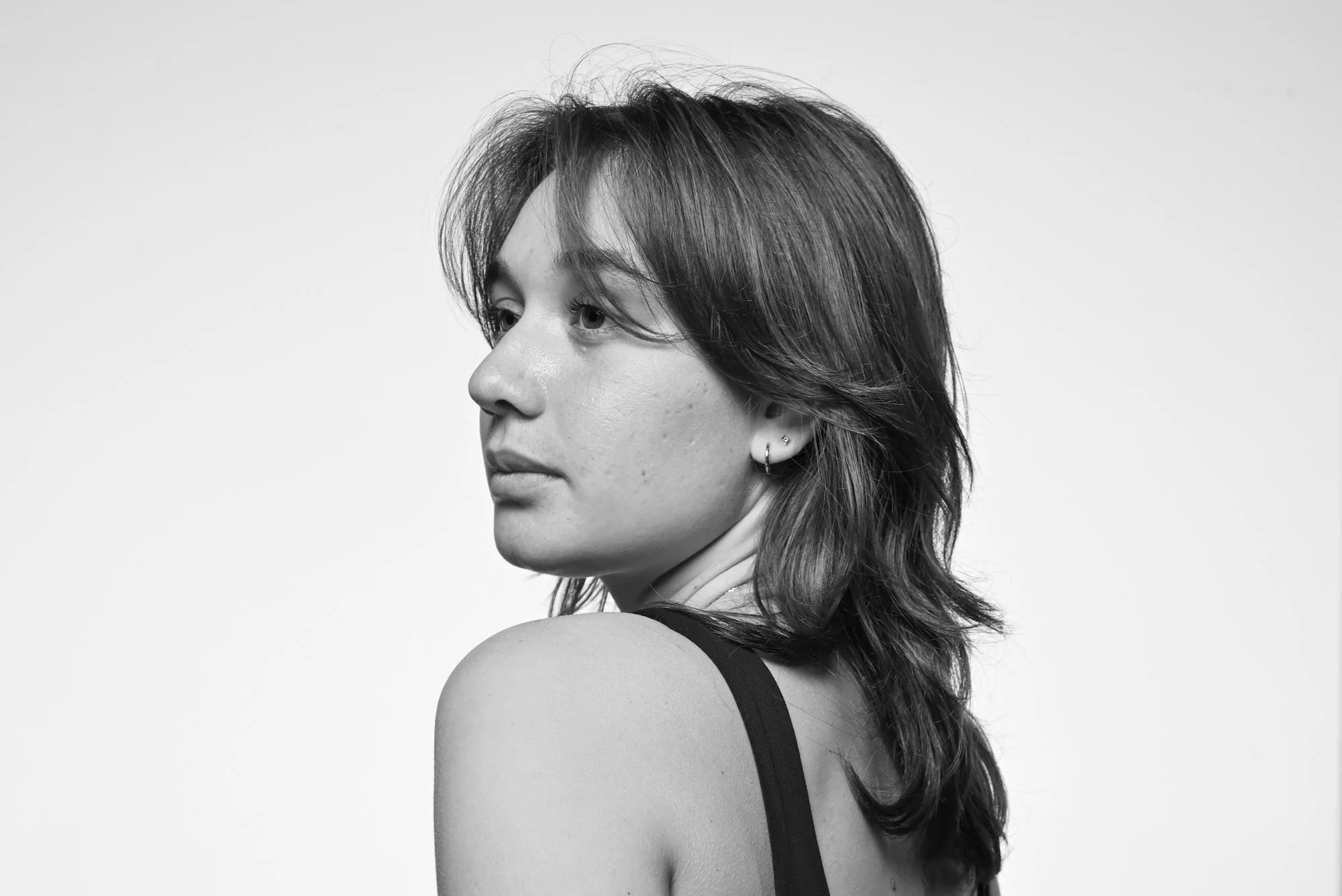 Black and white portrait of a young woman with shoulder-length hair, wearing a sleeveless top, looking to her left against a plain light background.