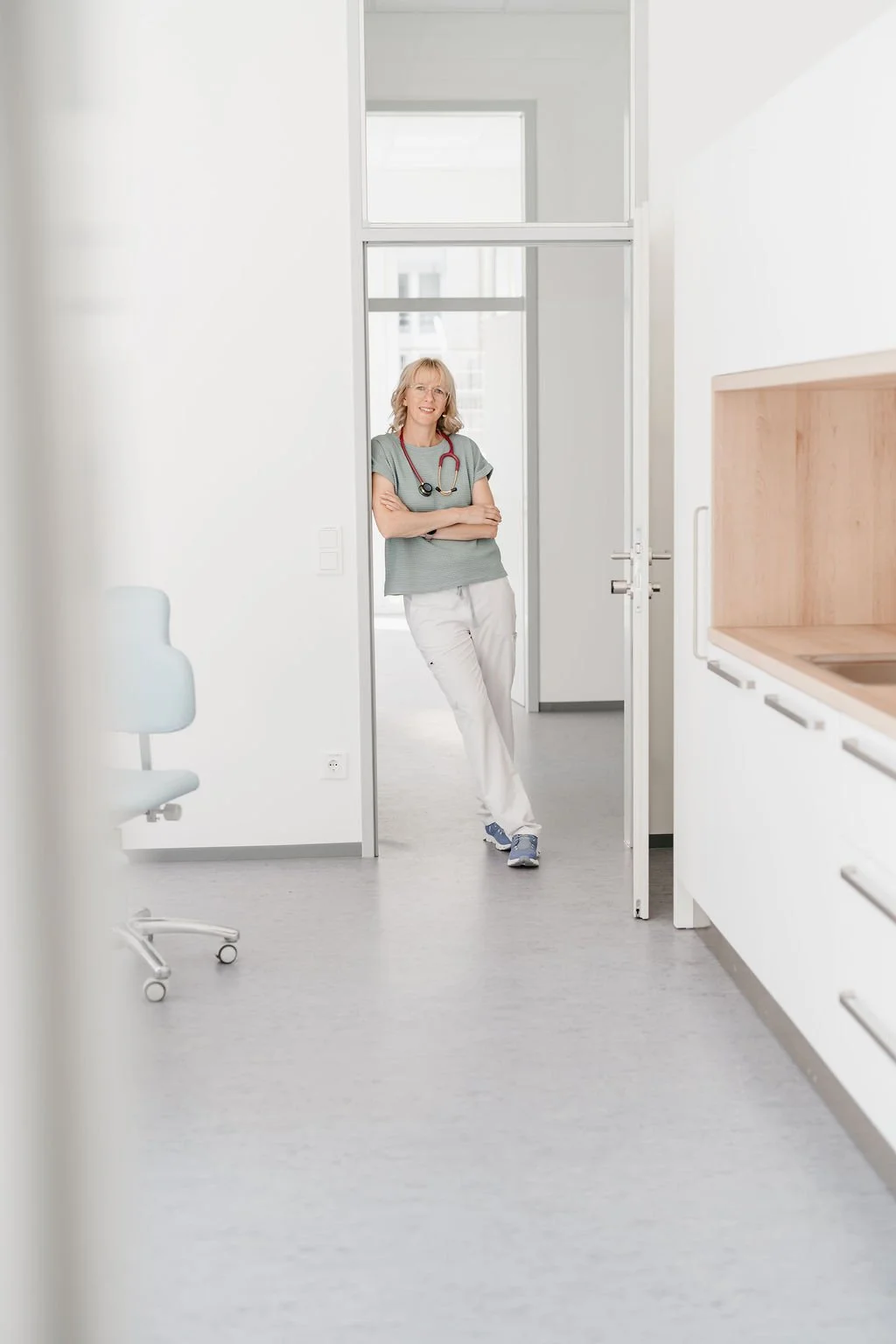 Dr. Judith Hirzenberger sitzt mit umgehängtem Stethoskop und blickt freundlich in die Kamera.