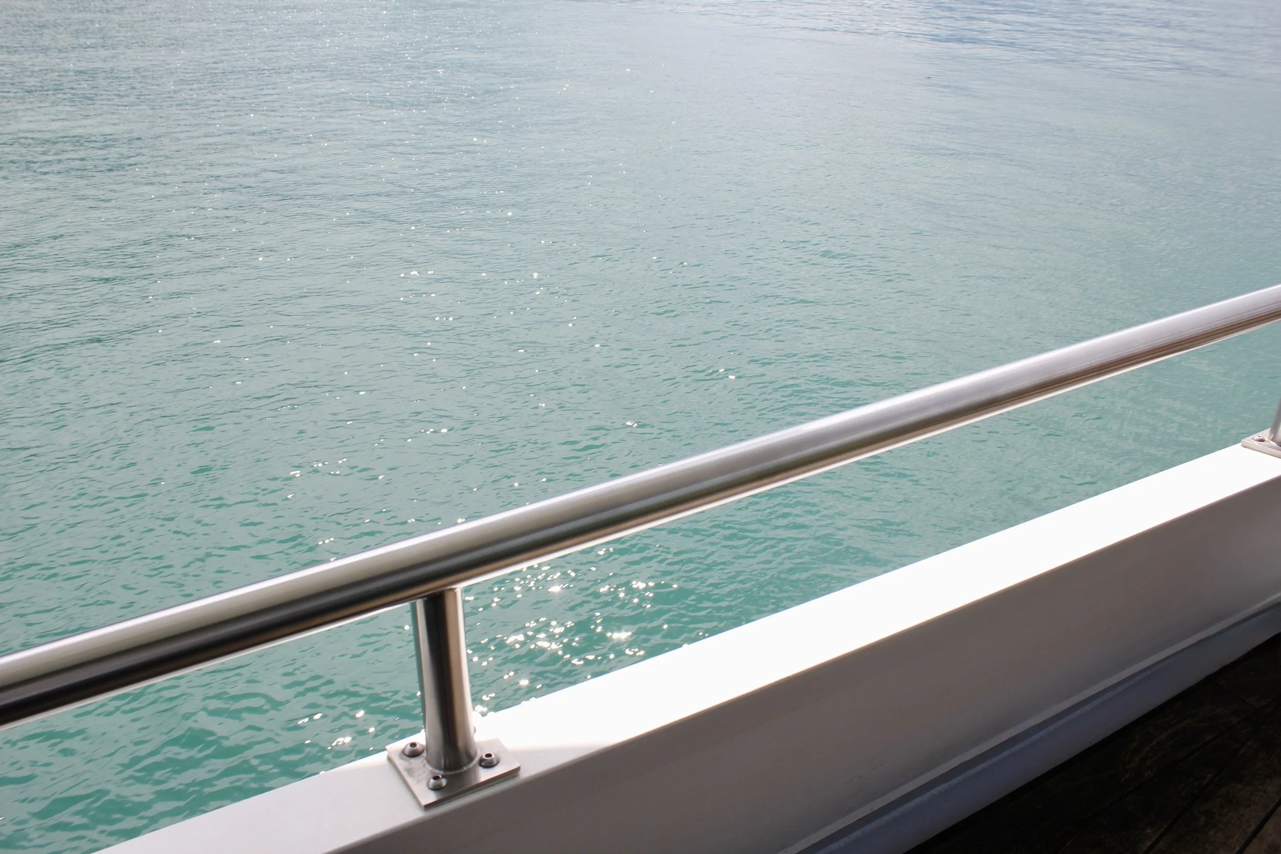 View of calm ocean water from the deck of a boat with a metal railing.