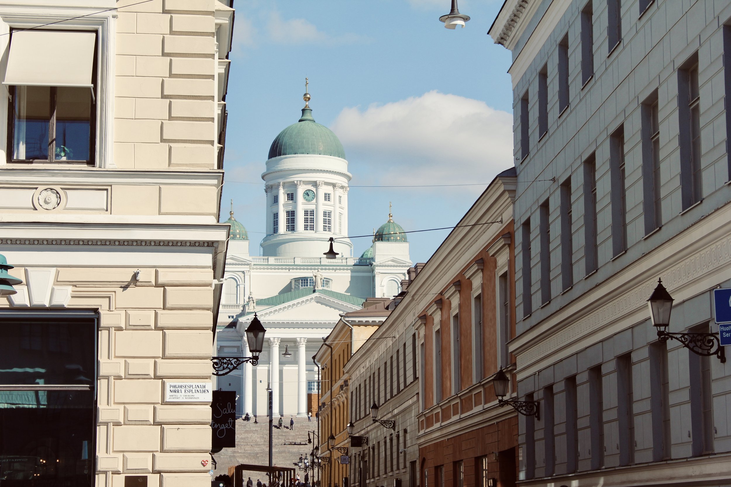 Street view of historic buildings with a large domed white church with smaller domes in the background.