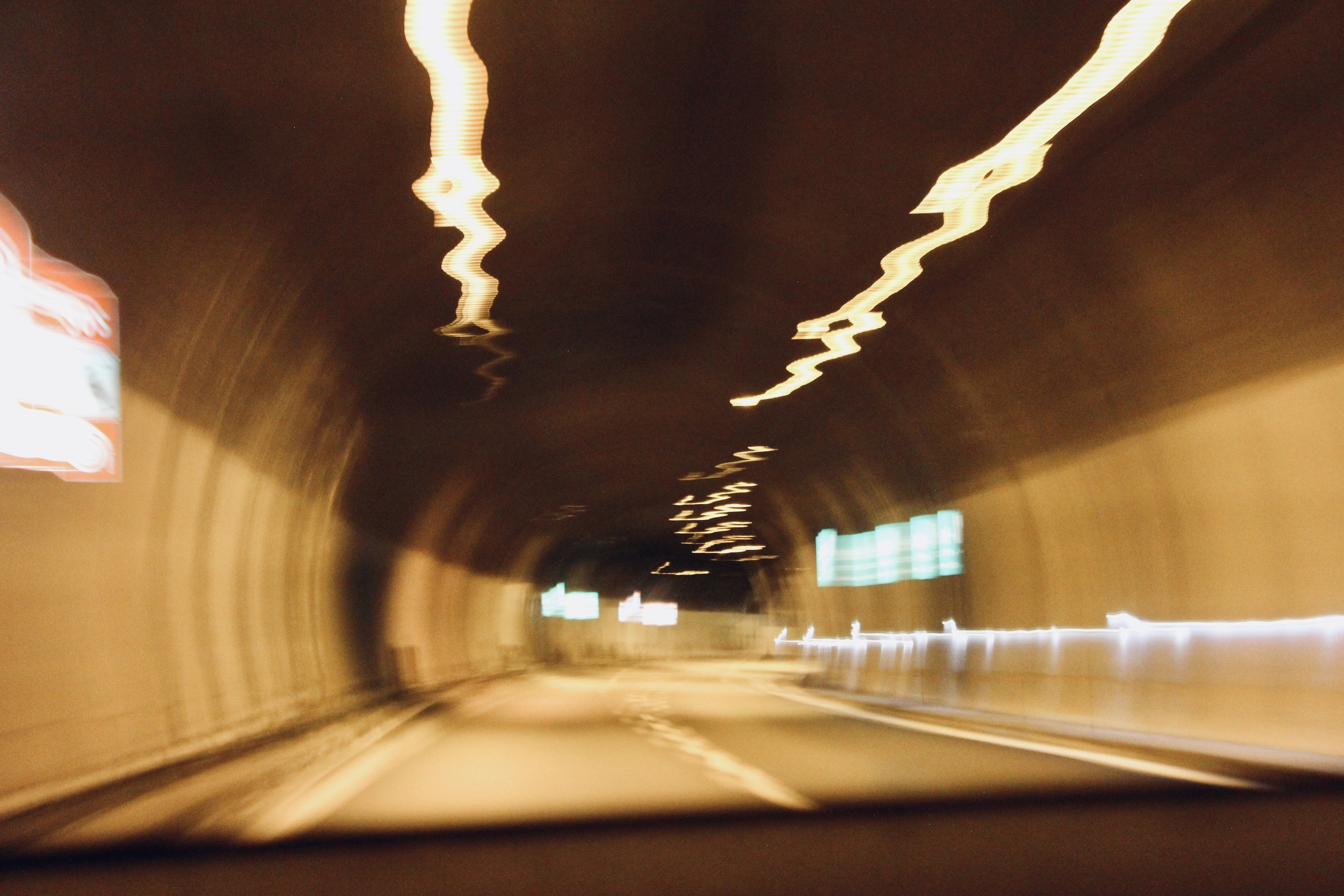 Blurred photo of a tunnel or underground passageway with wavy, zigzagging light reflections on the ceiling and illuminated signs on the walls.