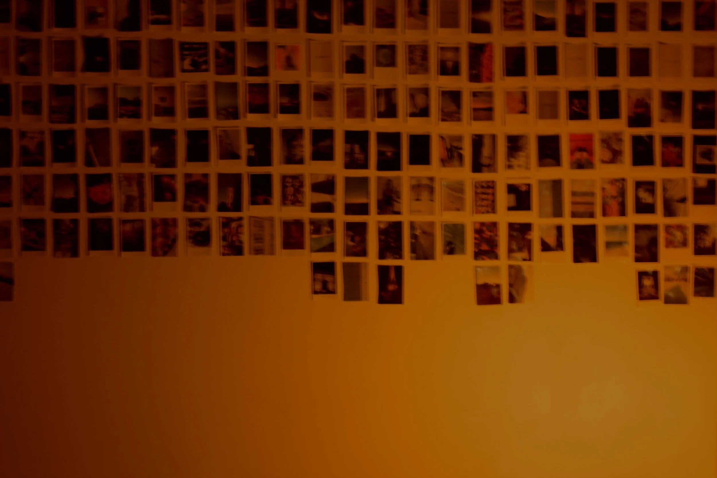 A collage of many small photographs arranged in rows and columns on a wall, with a warm orange background.